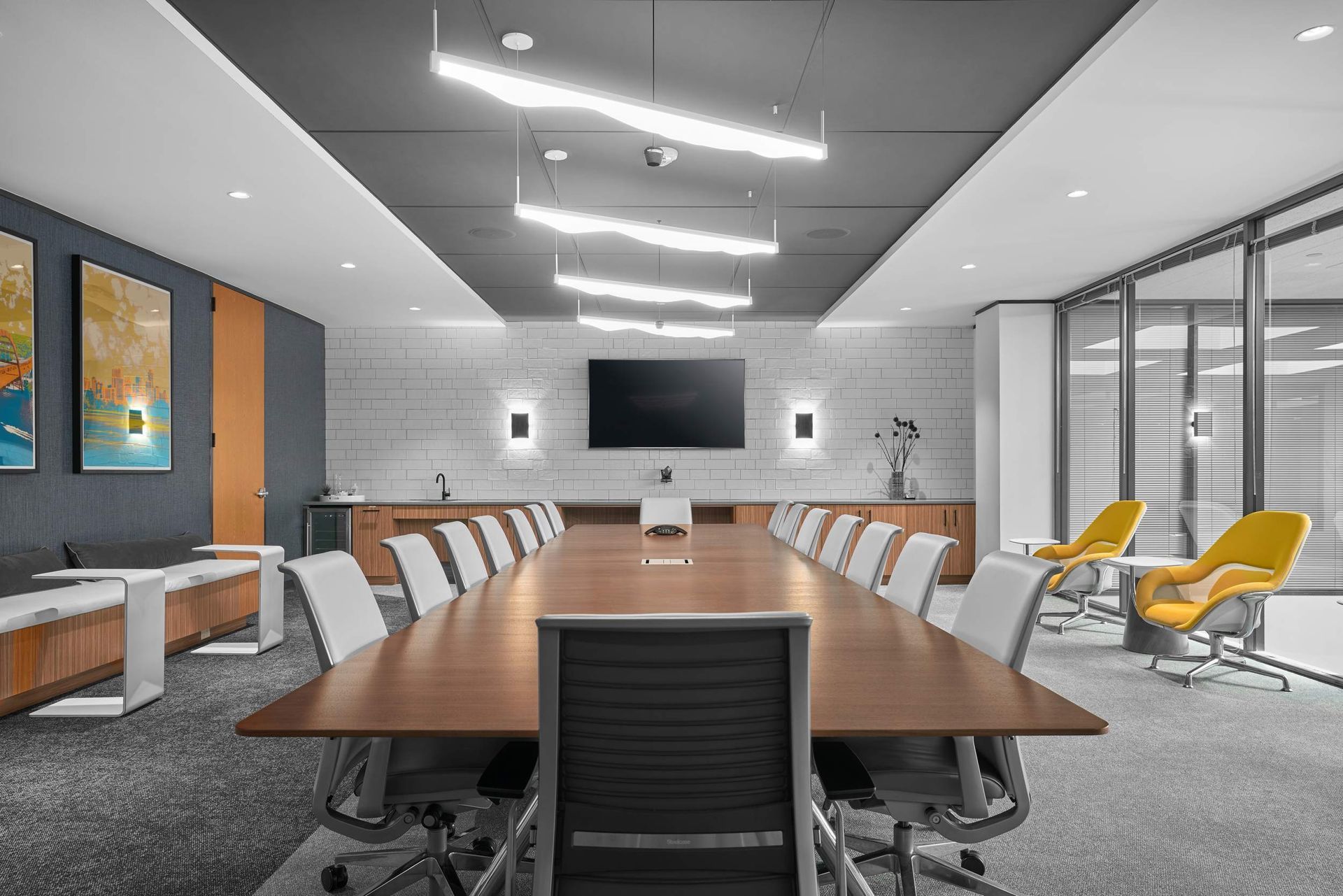 Conference room with long wooden table, chairs, TV, and modern lighting.