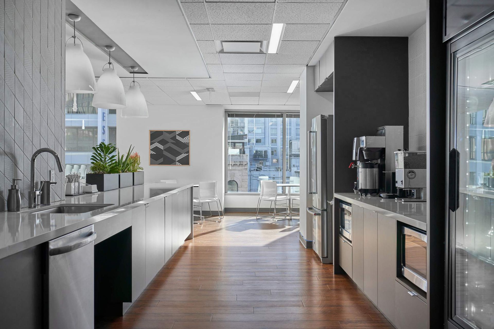 Modern office kitchen with long counters, appliances, and a window view.