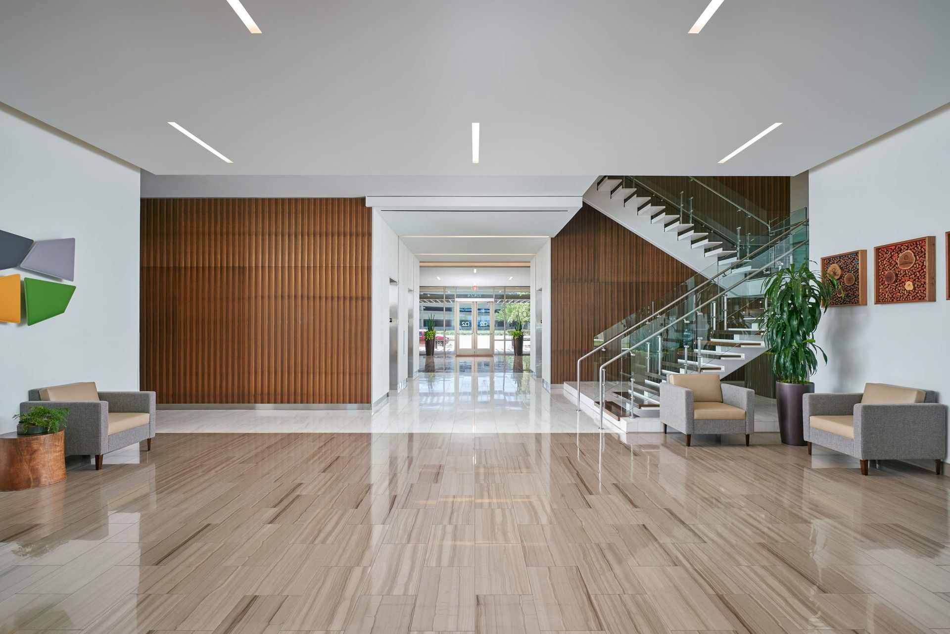 Spacious modern lobby with wood paneling, staircase, seating, and polished stone flooring.