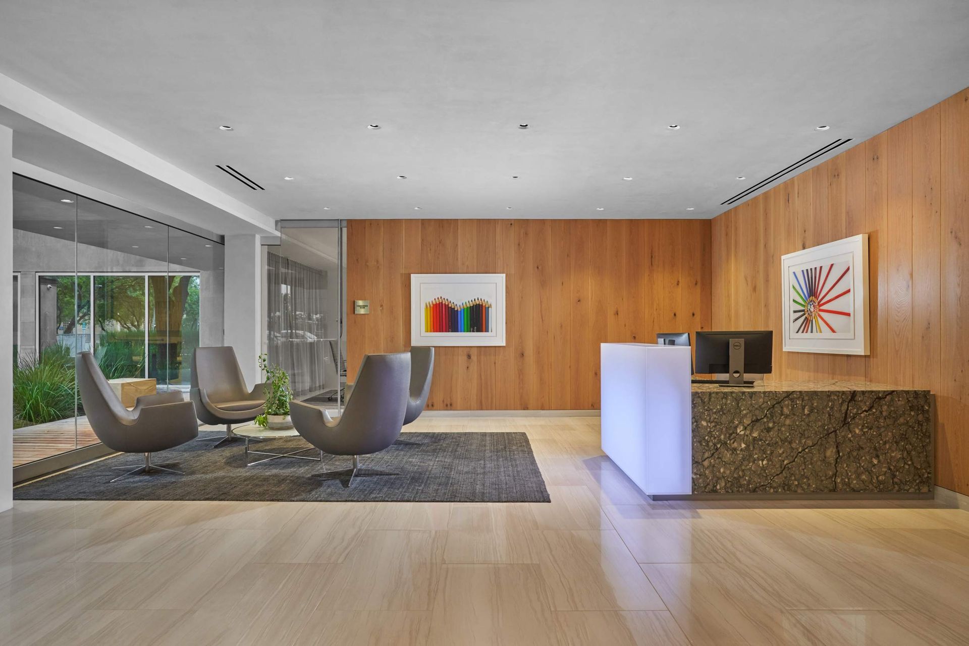Modern office reception area with wood paneling, artwork, and seating. Lighted reception desk.