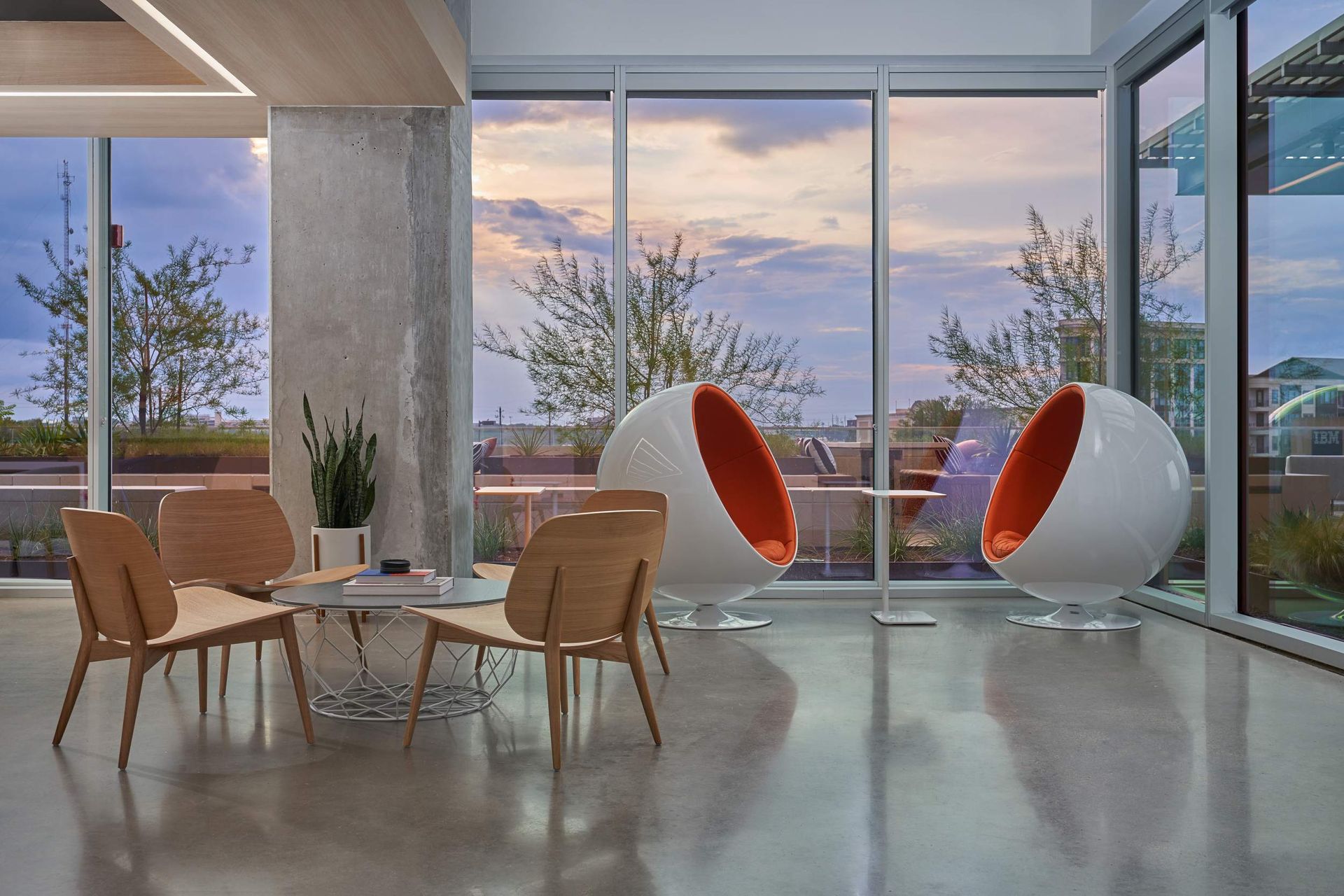 Modern lounge with round chairs and large windows overlooking a sunset.