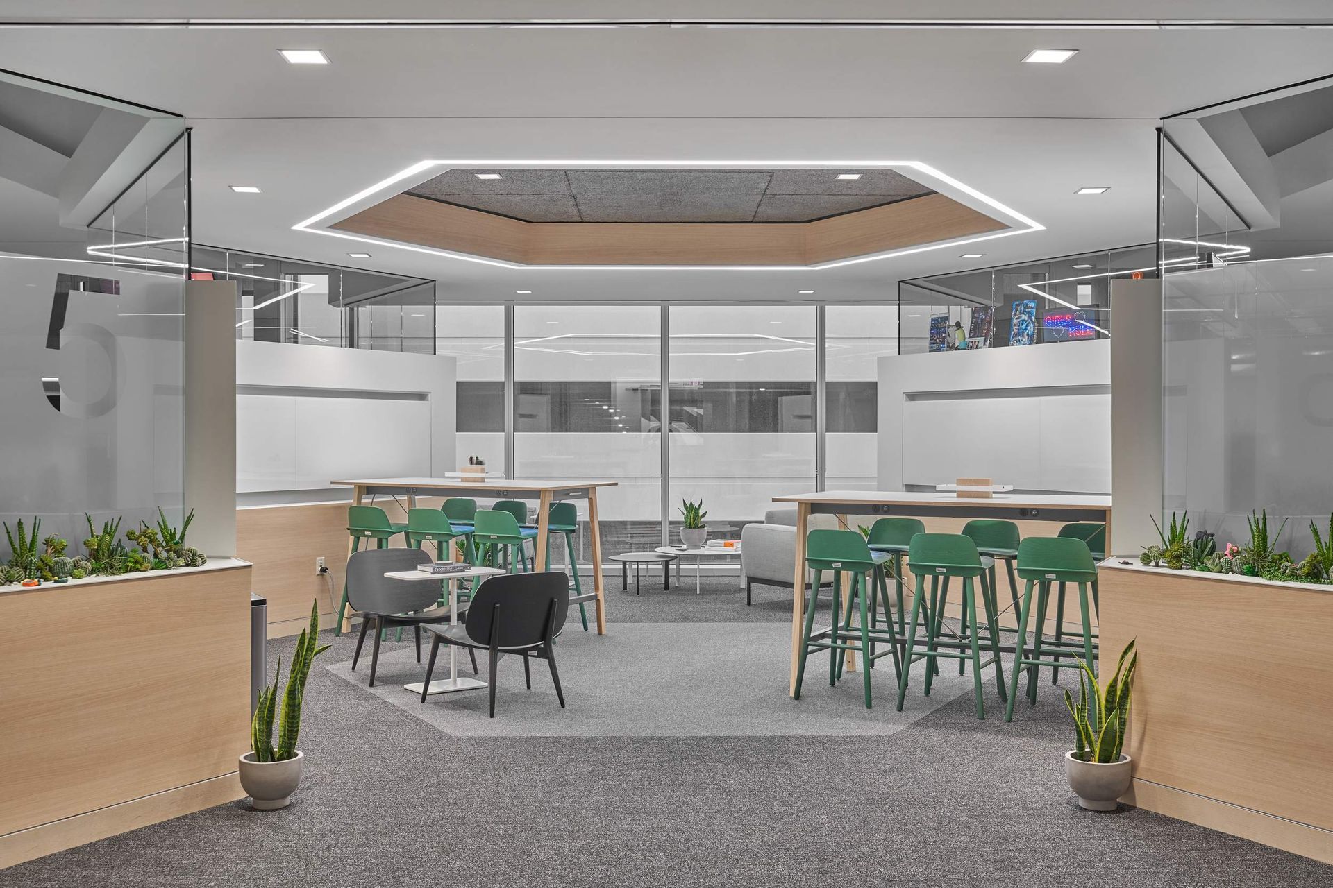 Modern office breakroom with green bar stools, tables, and plants. Light wood accents and an octagonal ceiling.
