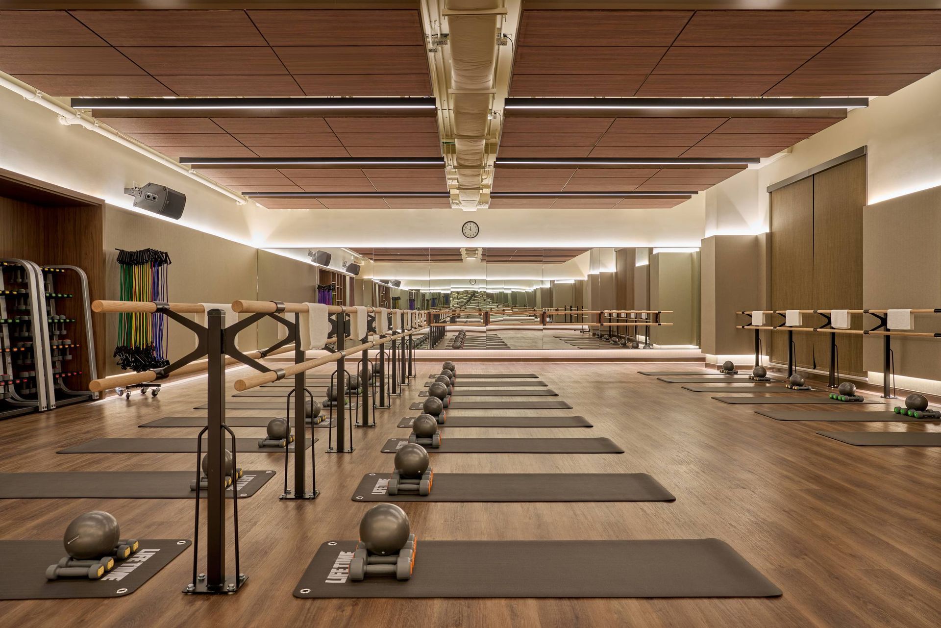 Empty barre studio with mats, weights, and ballet barres, with wood accents and mirrored wall.