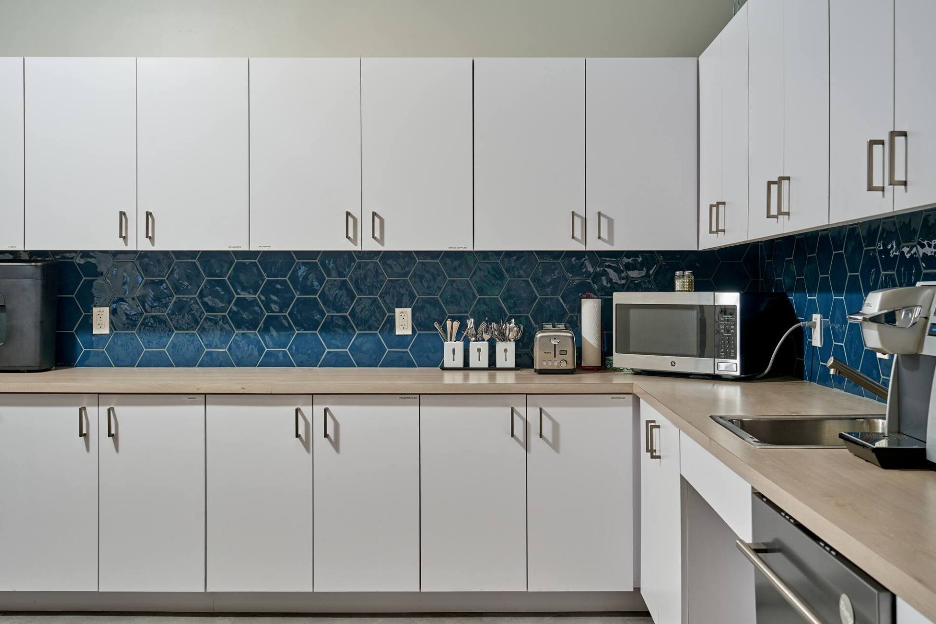 White kitchen cabinets with blue tile backsplash; microwave, toaster, and coffee maker on the counter.