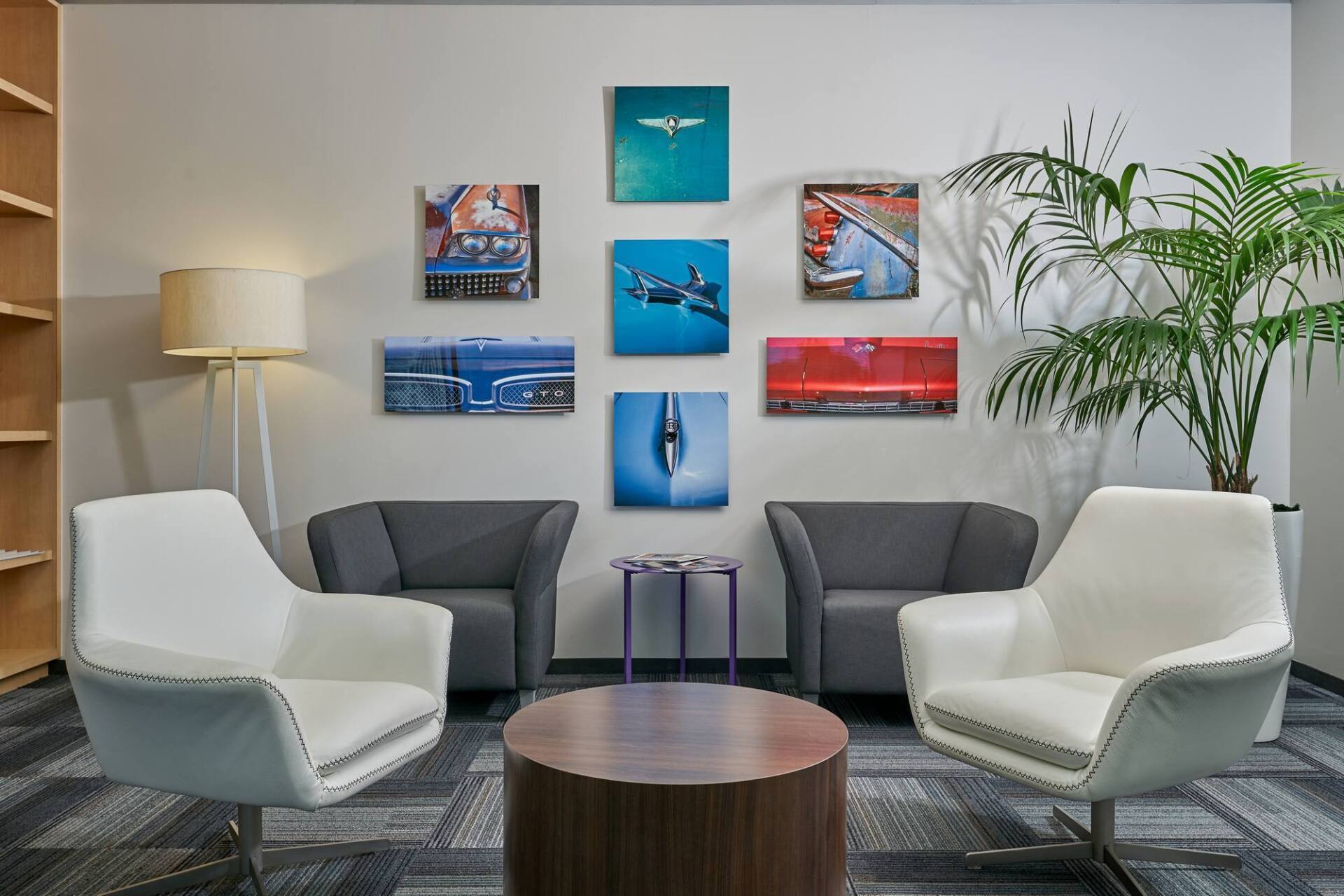 Lounge area with white chairs, gray sofa, and artwork on the wall. A potted plant stands nearby.