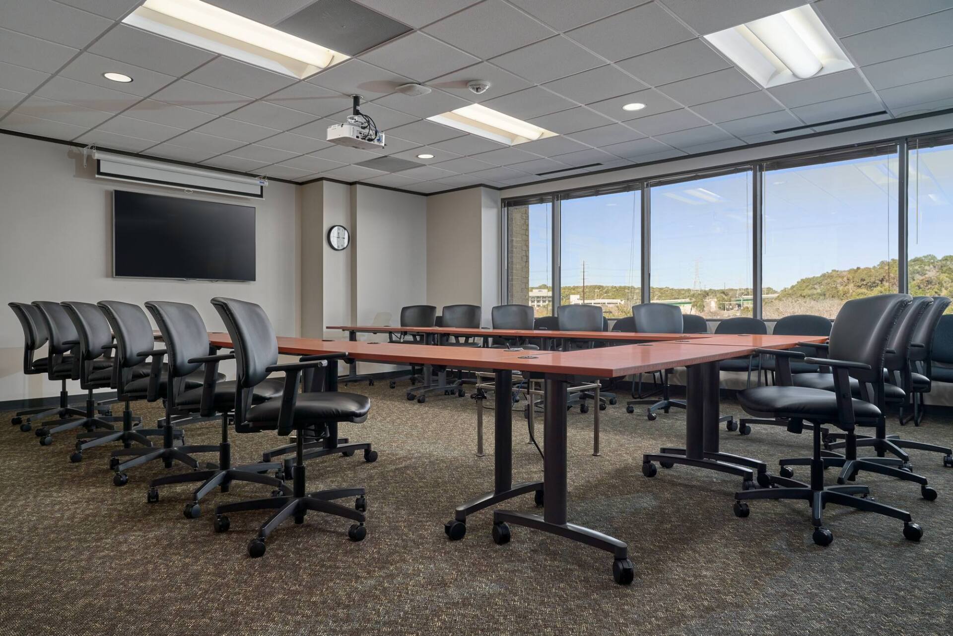 Conference room with brown tables, black chairs, large screen, and window view.