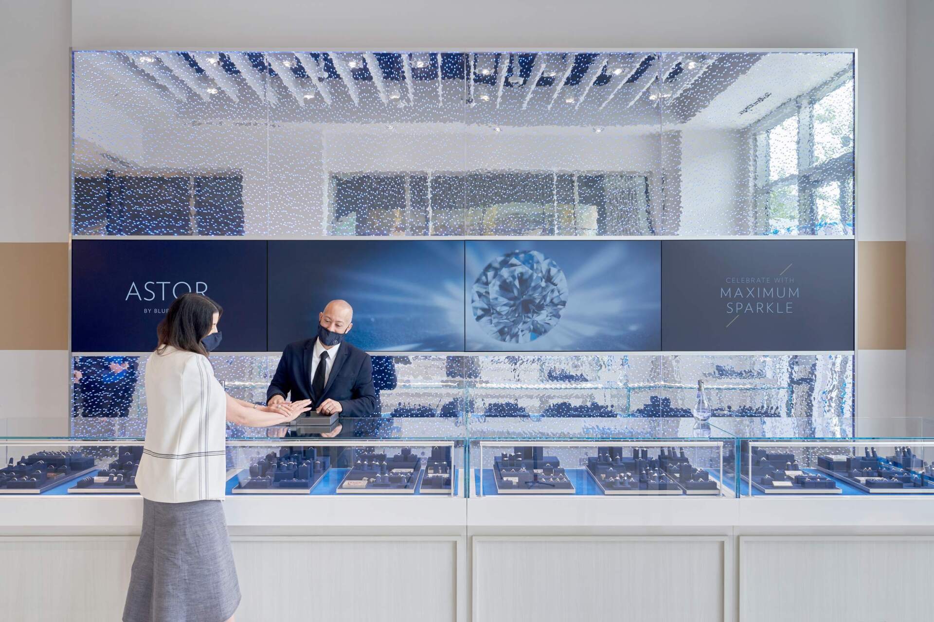 Customer and salesperson in a jewelry store with display cases and large mirrored wall.