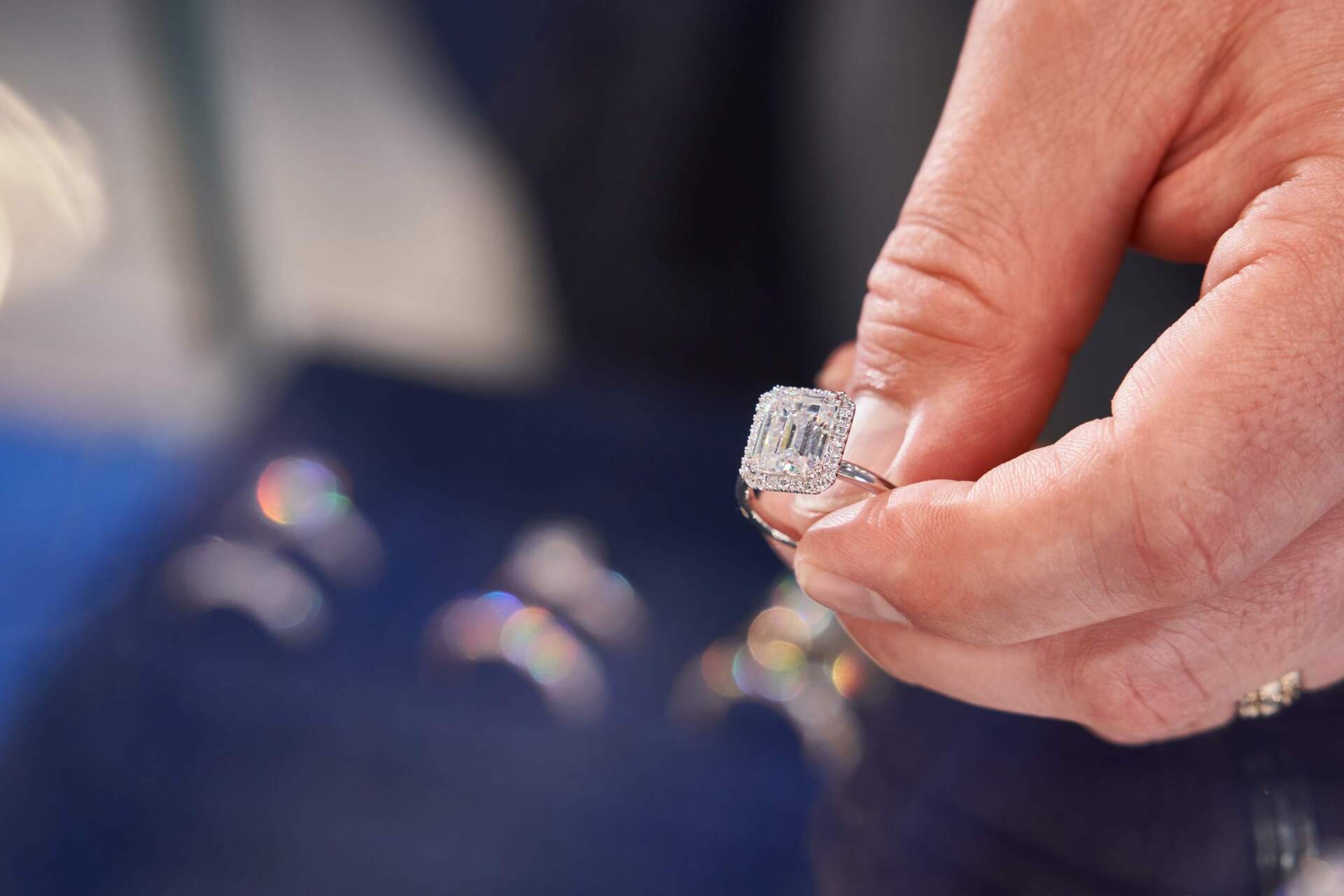 Hand holding diamond engagement ring. Blue reflective surface in background.