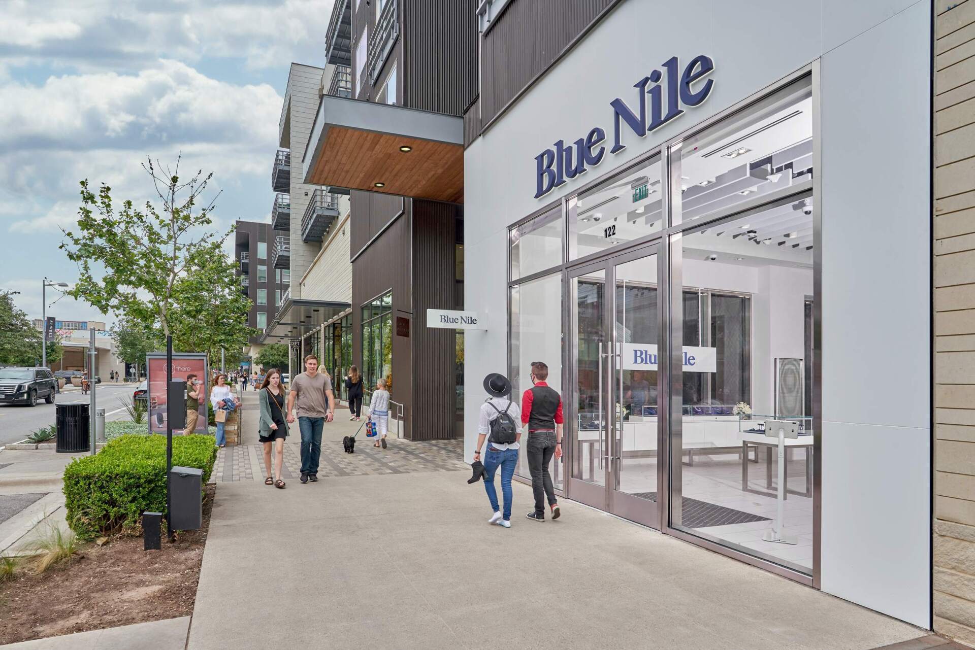 Blue Nile jewelry store front with glass doors, sidewalk, and pedestrians. Modern architecture with sign.