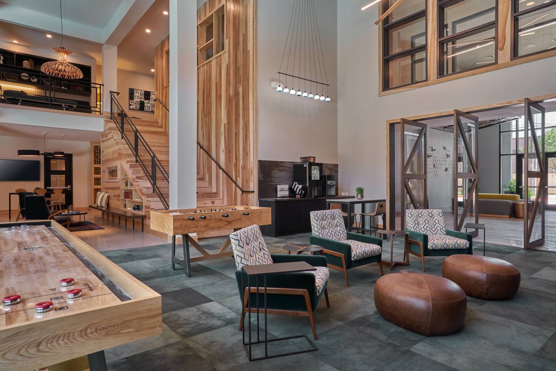 Lobby with shuffleboard, foosball, seating, and a staircase. Wooden accents, neutral colors, and natural light.