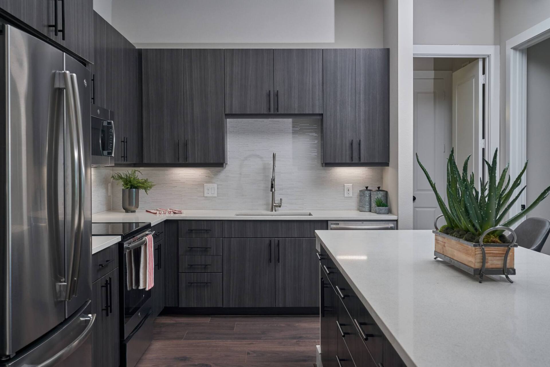 Modern kitchen with dark wood cabinets, stainless steel appliances, and white countertop island.
