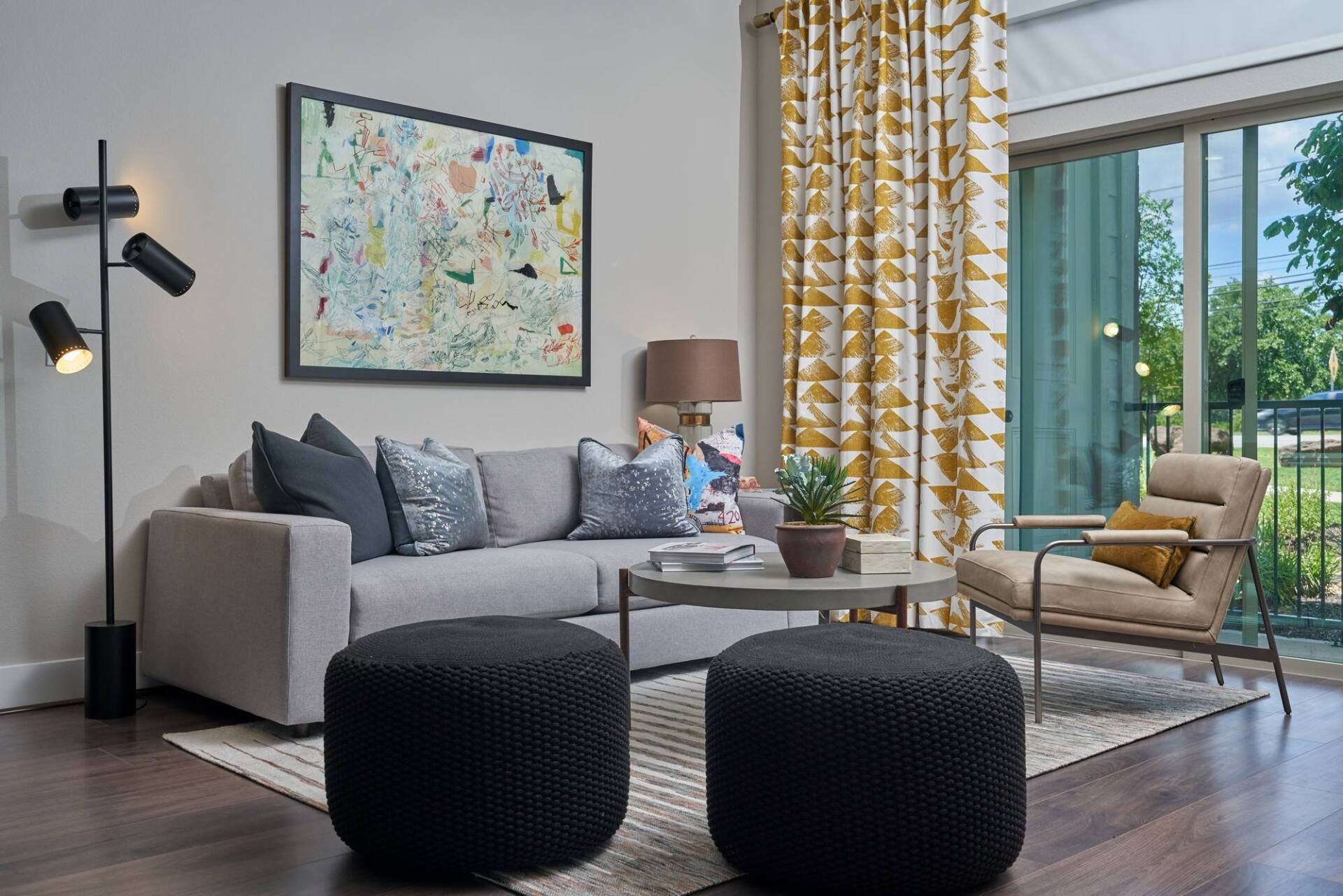 Living room with gray sofa, abstract art, floor lamp, and patterned curtains.
