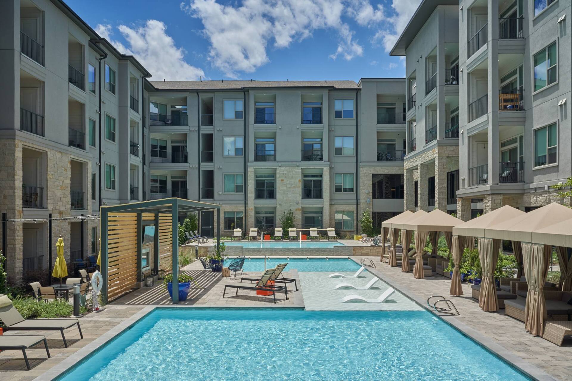 Pool and lounge area in a courtyard surrounded by multi-story apartment buildings.