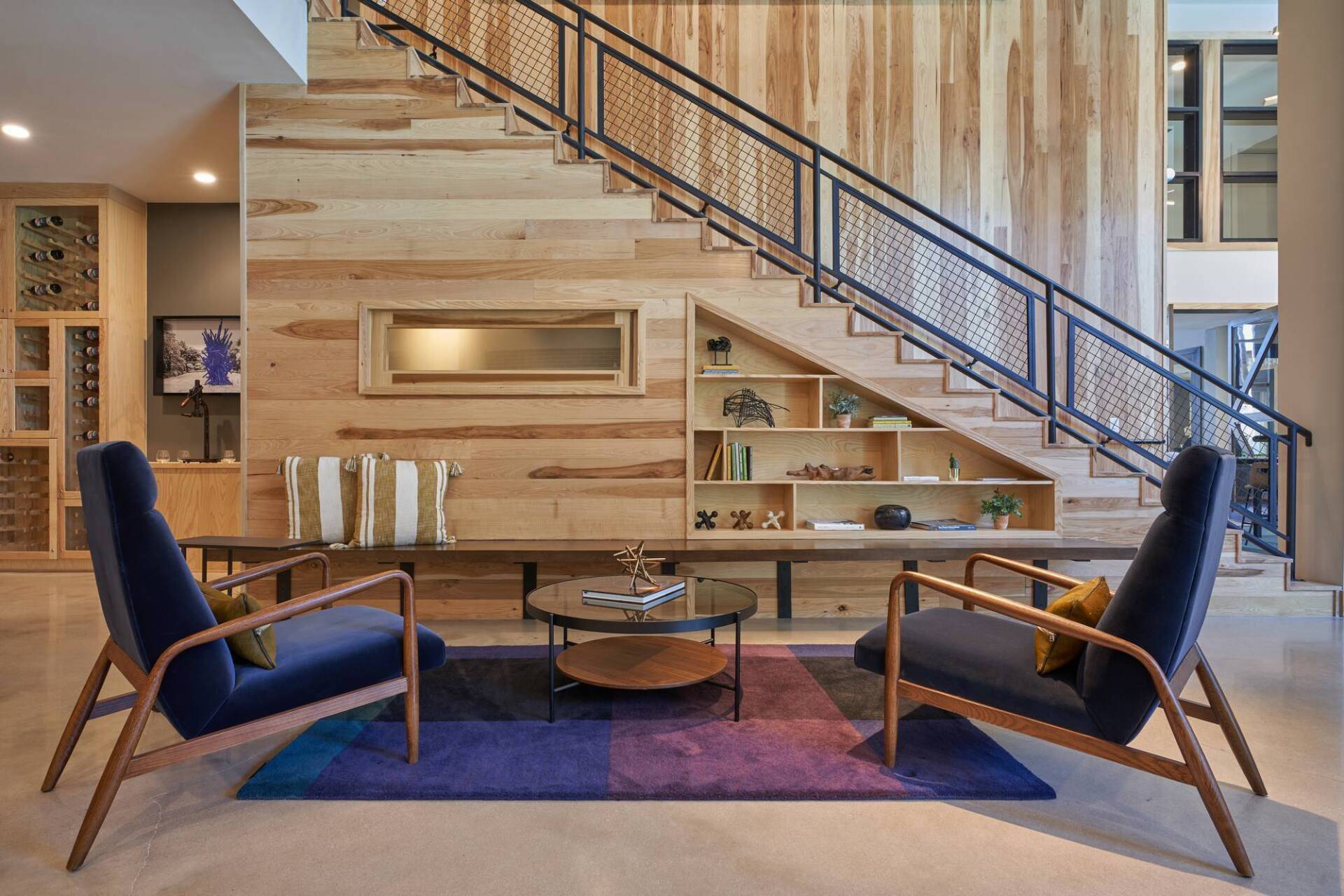 Modern interior with wood-paneled wall, staircase, and seating area with two blue armchairs.