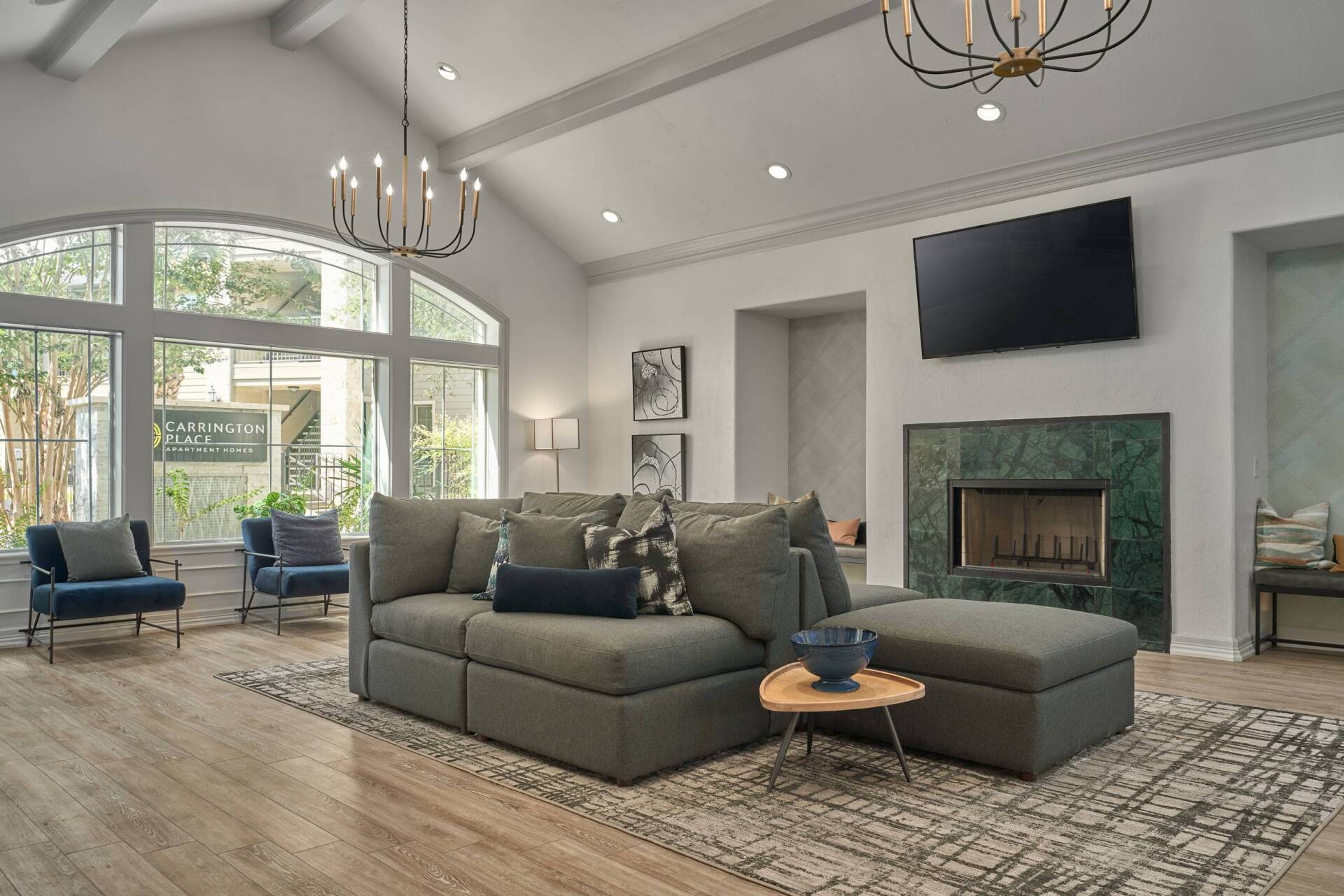 Spacious living room with gray sectional, fireplace, large windows, and chandeliers.
