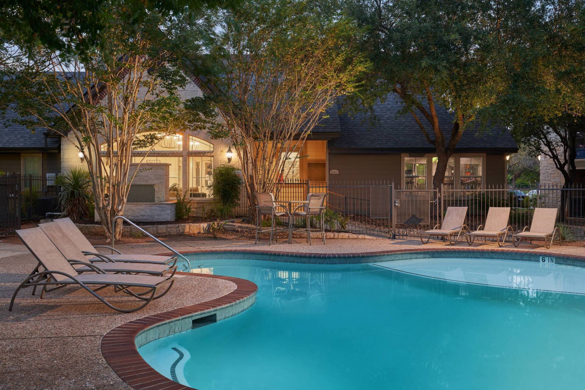 Swimming pool with lounge chairs, trees, and building at dusk.