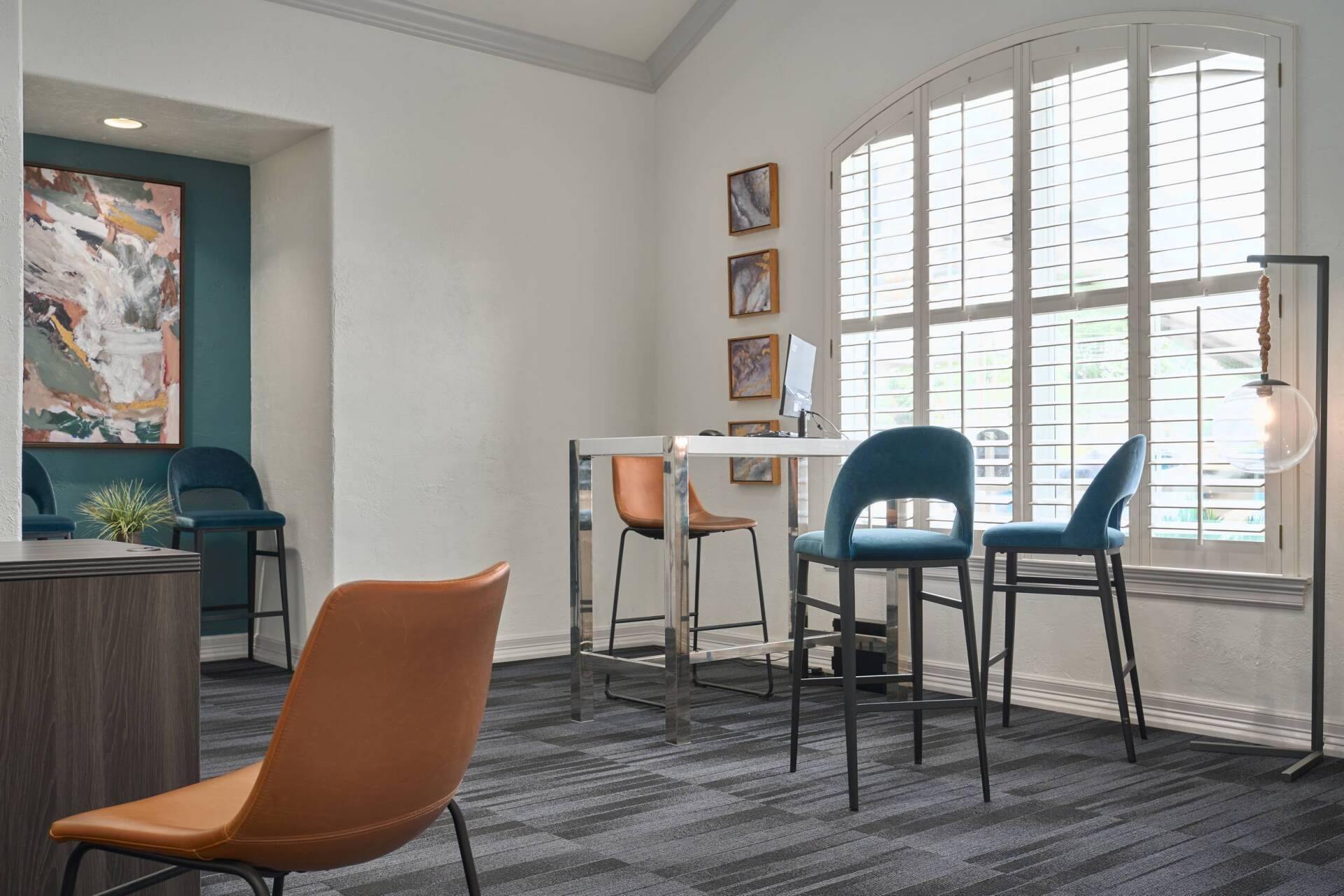 Modern office waiting area with chairs and table near a large window, artwork on wall.