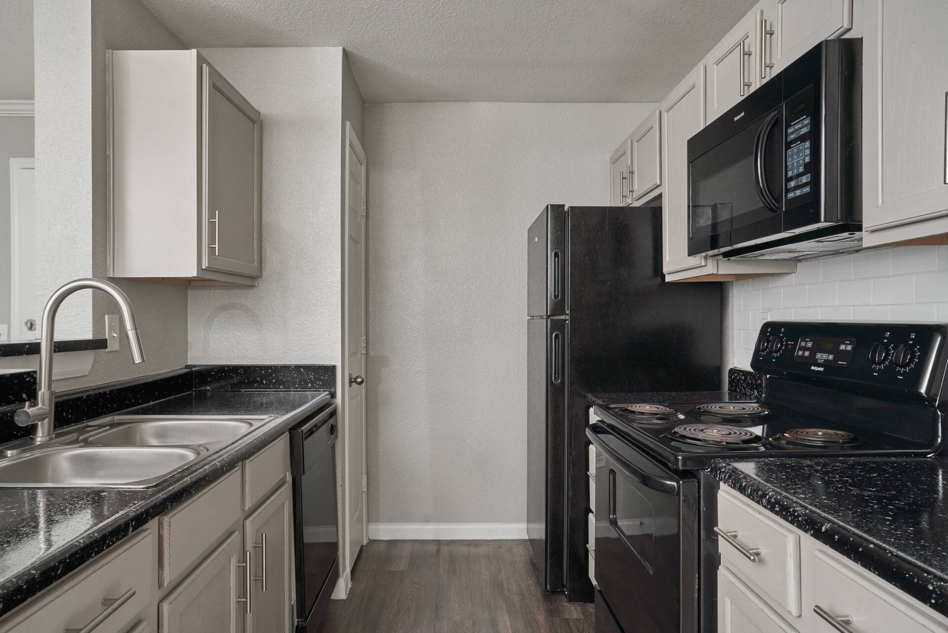 Kitchen with grey cabinets, black countertops and appliances; includes a refrigerator, microwave and stove.