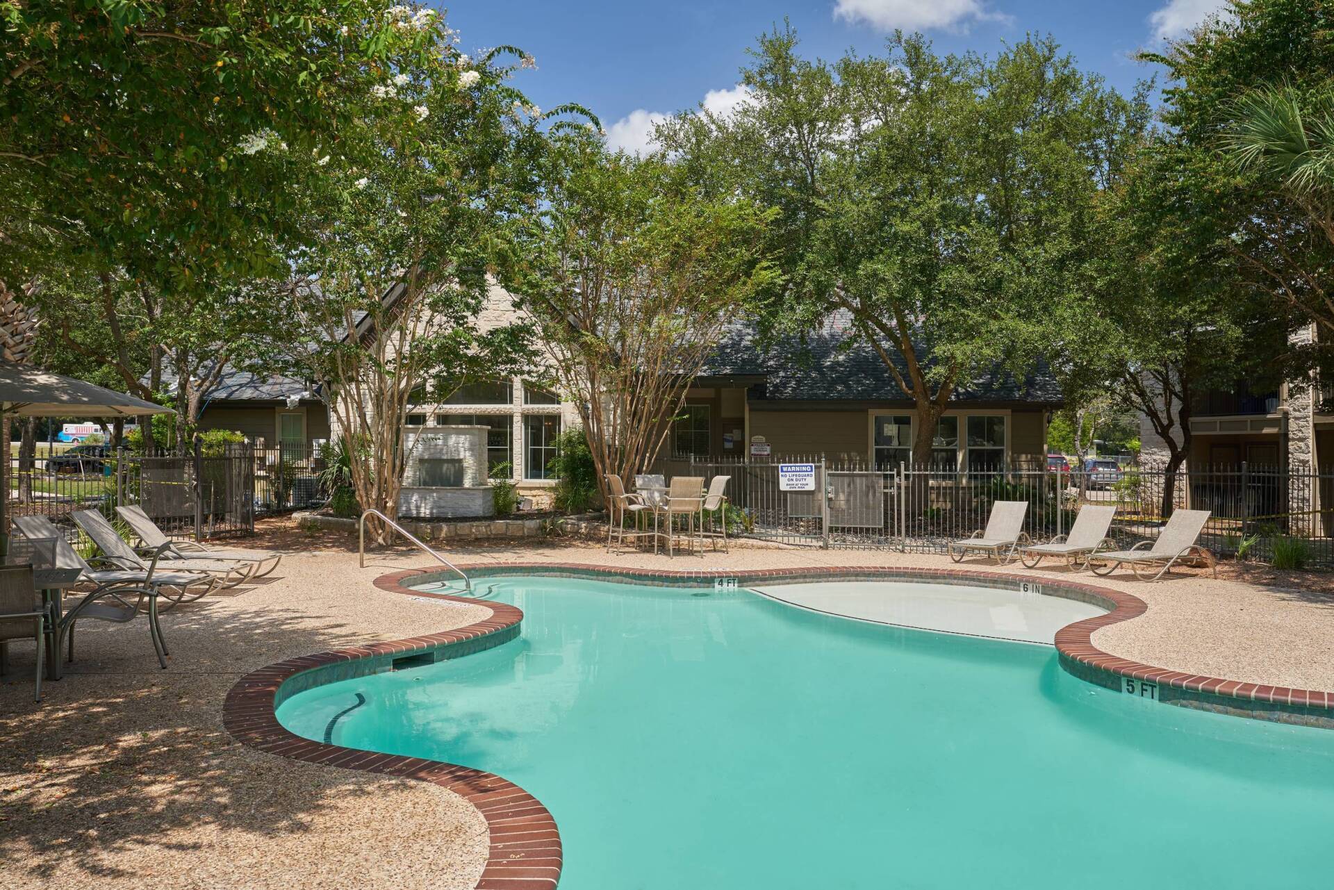 Swimming pool surrounded by trees, with lounge chairs and tables on the deck.
