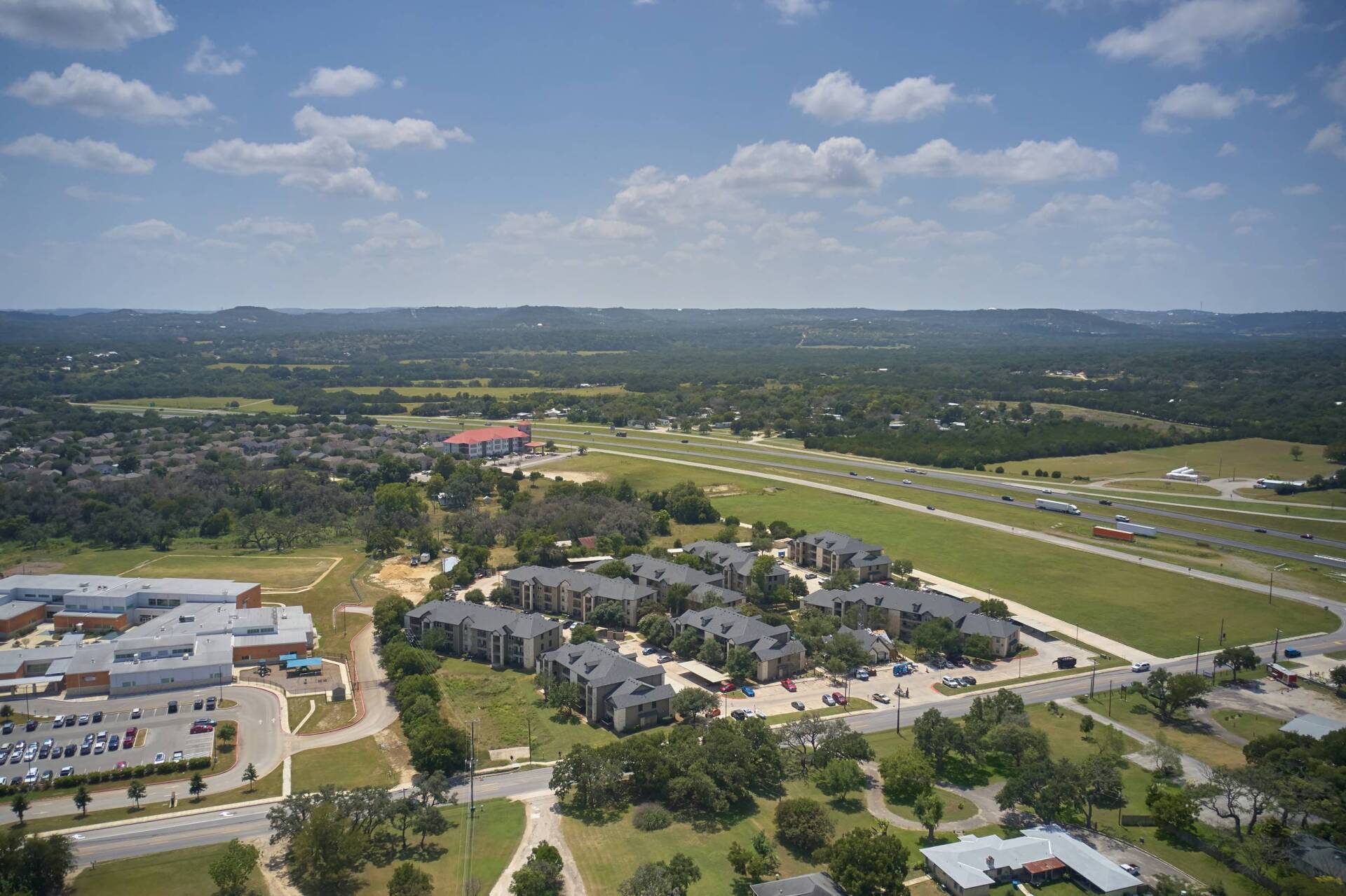 Aerial view of buildings, green fields, and a long airstrip under a bright blue sky.