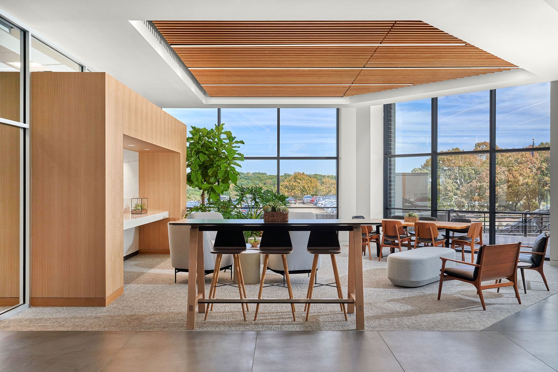 Modern office lounge with wooden accents, large windows, and various seating areas.