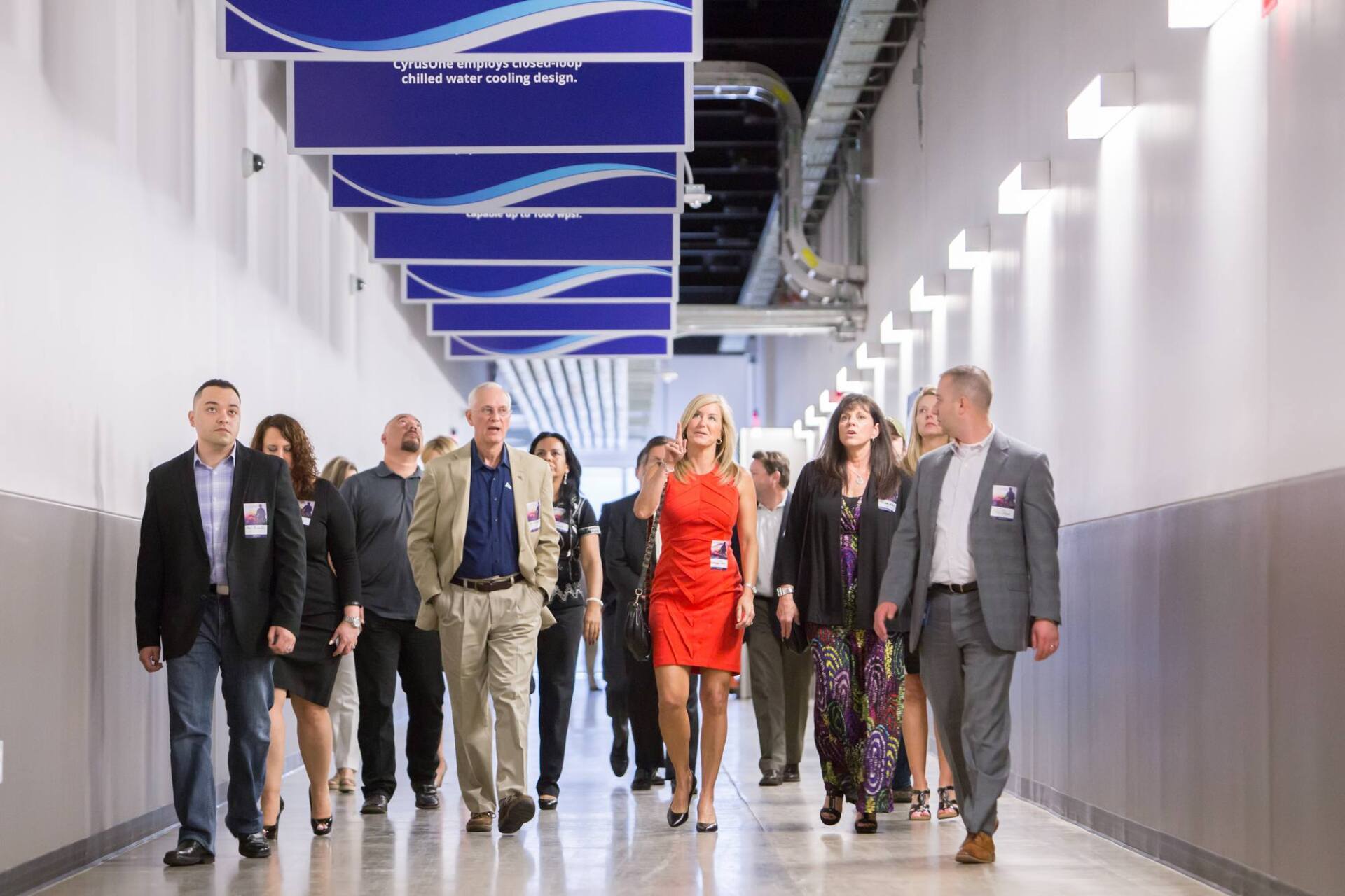 Group of people walking down a long, white hallway with blue overhead signs.