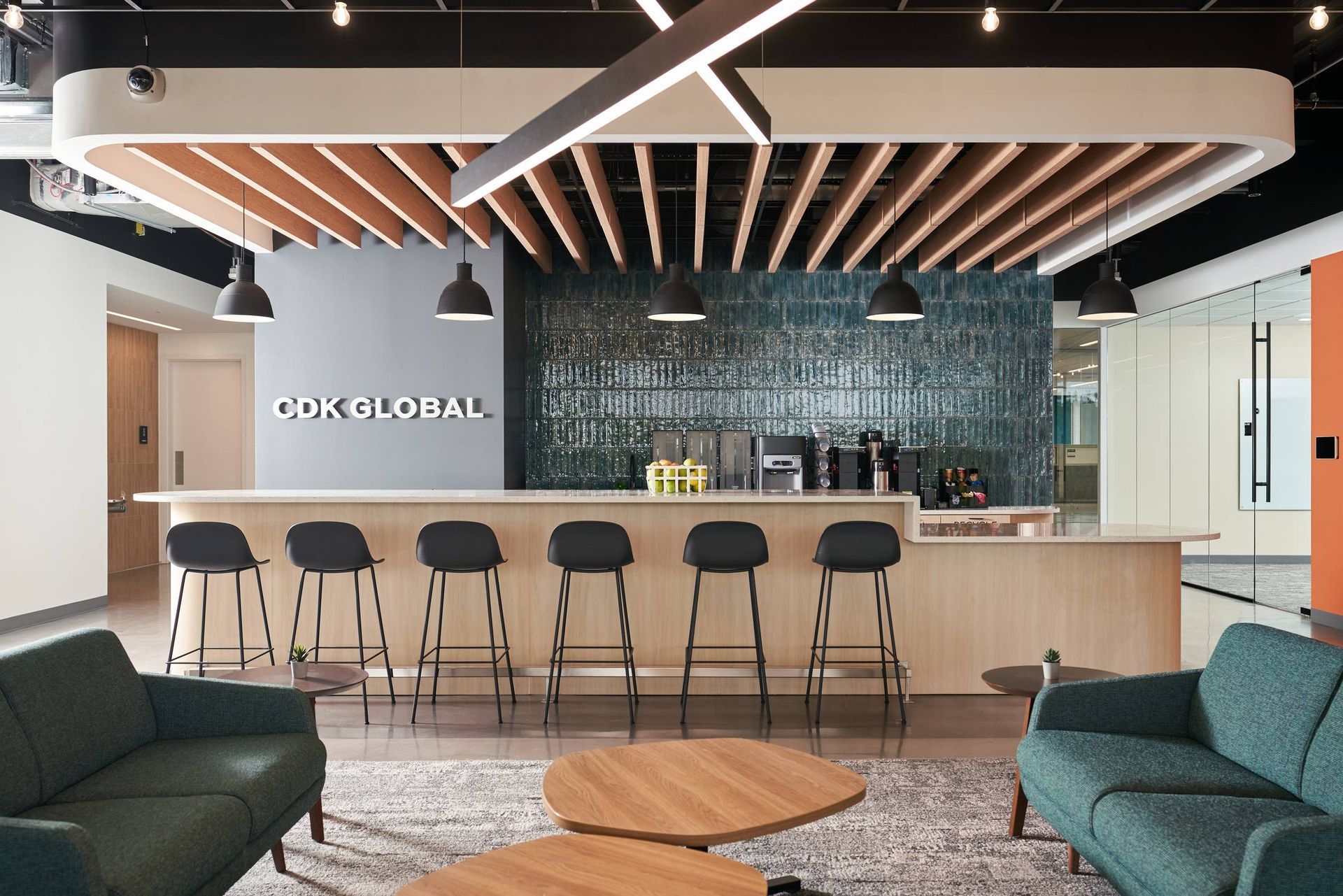 Modern office lounge with bar seating, teal couches, and a wood ceiling feature.