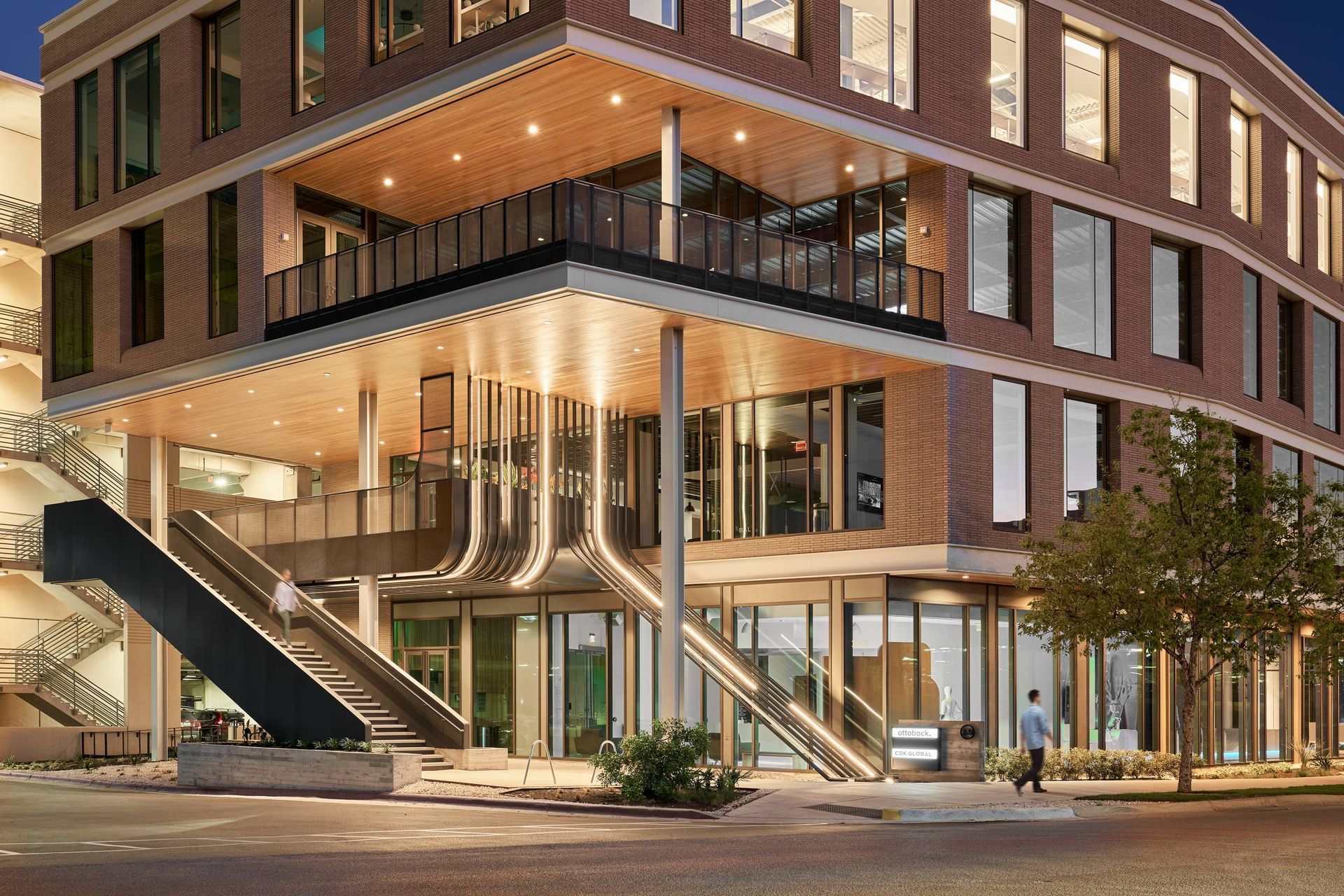 Modern brick building with glass windows, entrance canopy, and outdoor staircase.