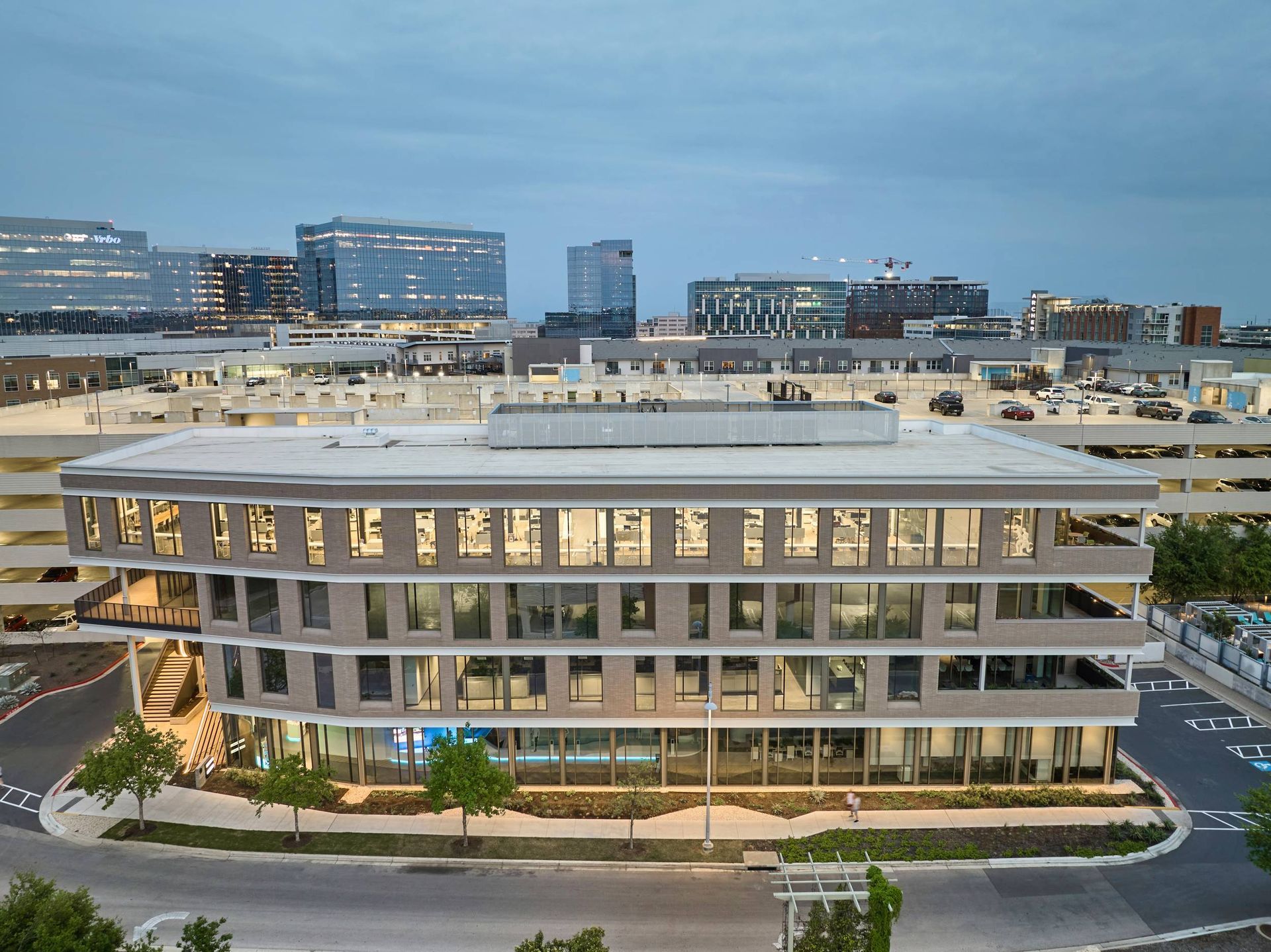 Aerial view of a modern, multi-story office building with a curved facade; cityscape background.