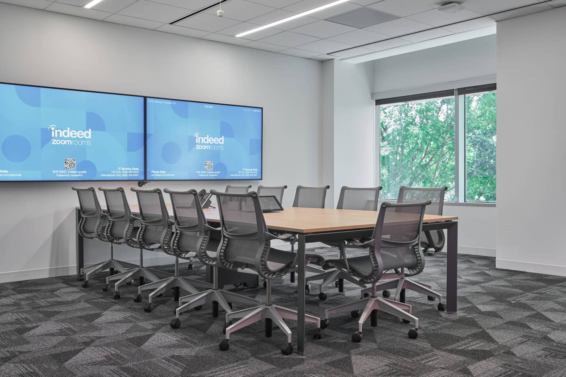 Conference room with a long table, chairs, large screens displaying
