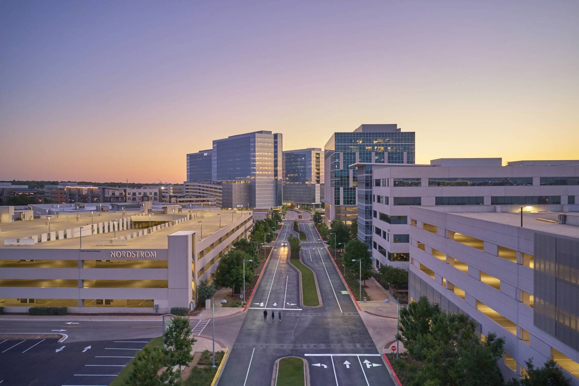 Road between tall buildings at dusk. Blue and tan buildings. Sunset.