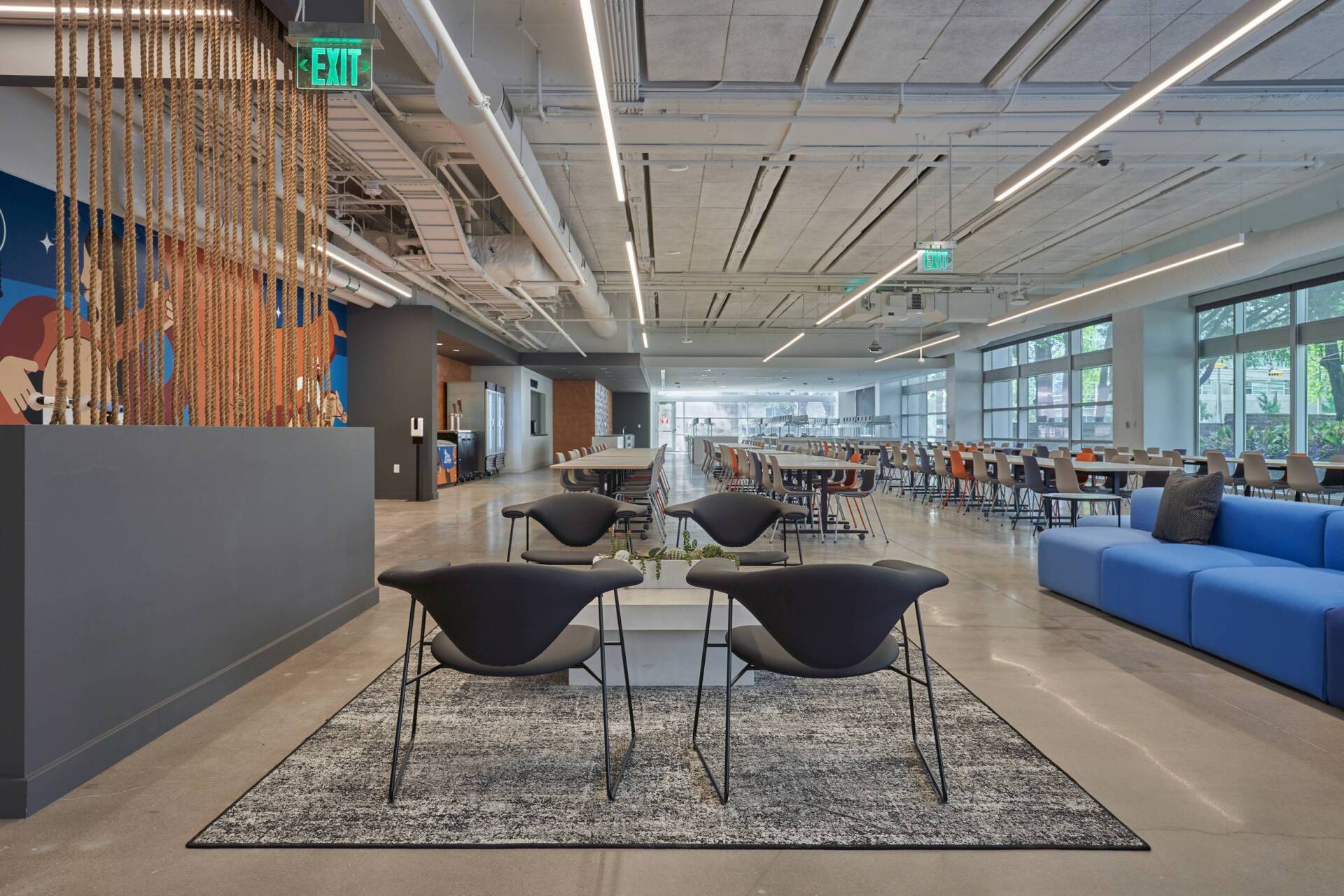 Modern office lounge with seating areas, tables, and a long hallway, illuminated by overhead lighting.