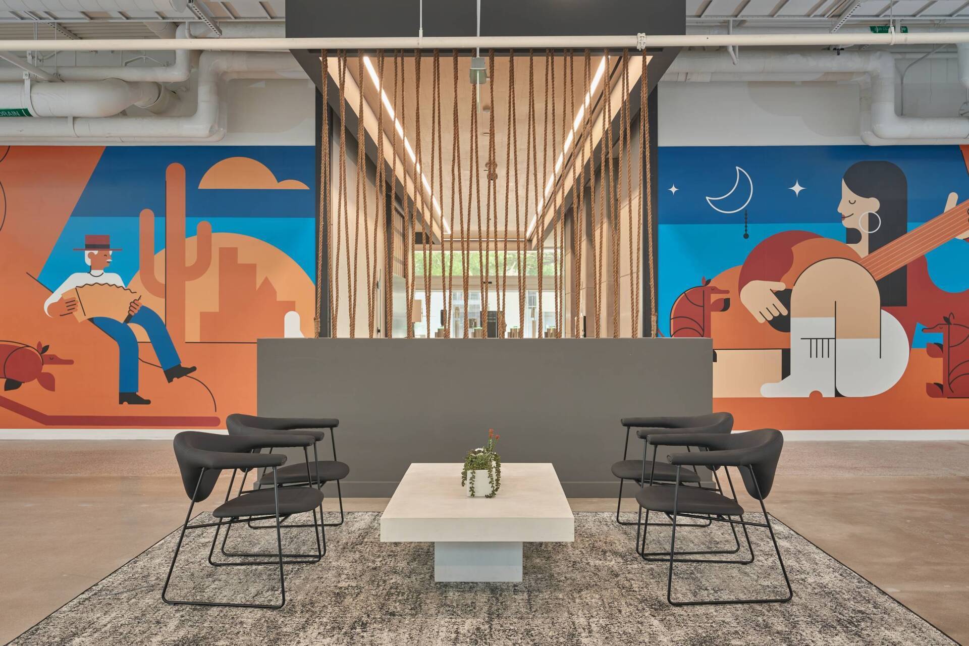 Lobby with gray chairs, coffee table, and mural. Wooden accents around a reception desk with people in the artwork.