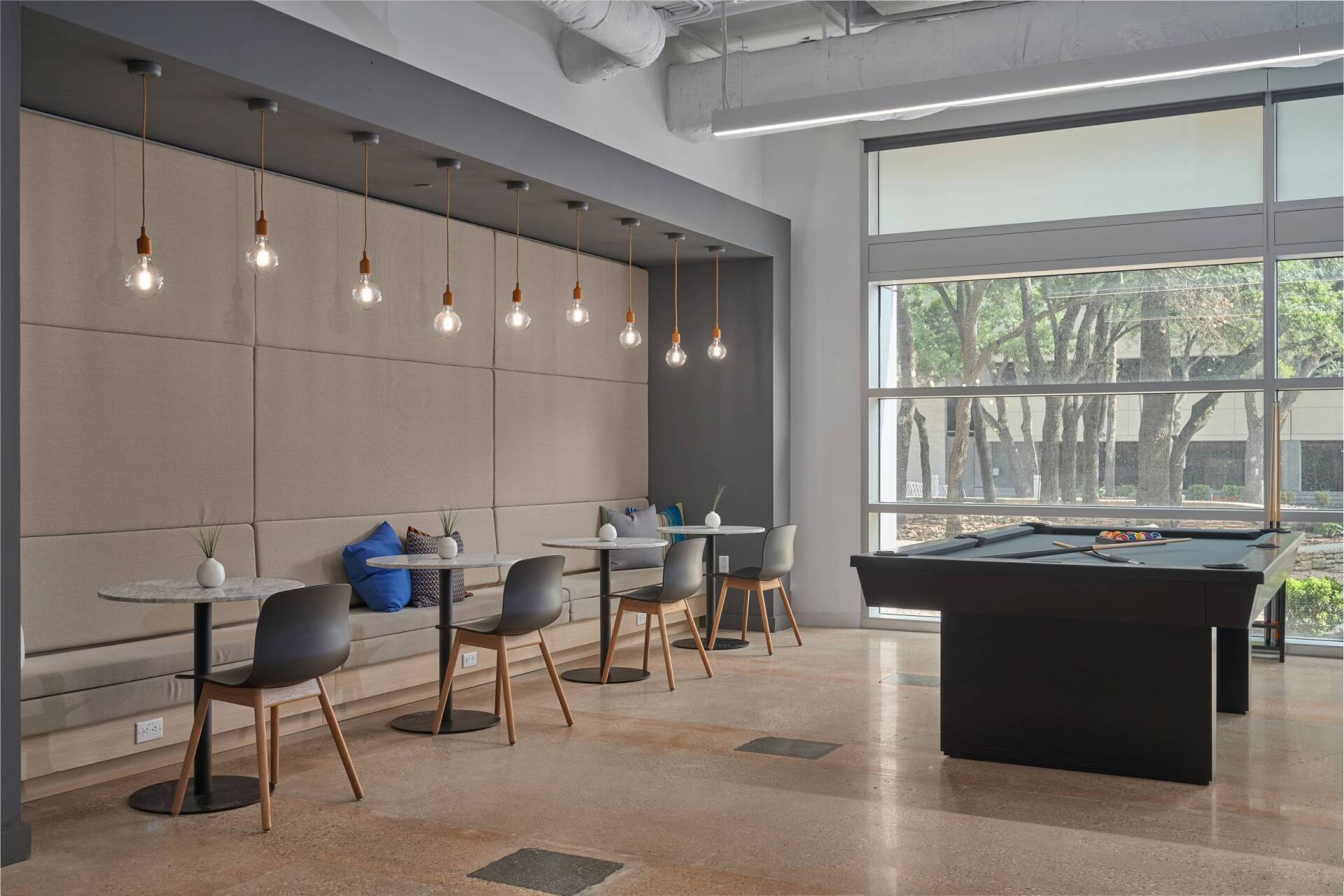 Lounge area with a built-in bench, tables, chairs, pendant lights, and a pool table near a large window.