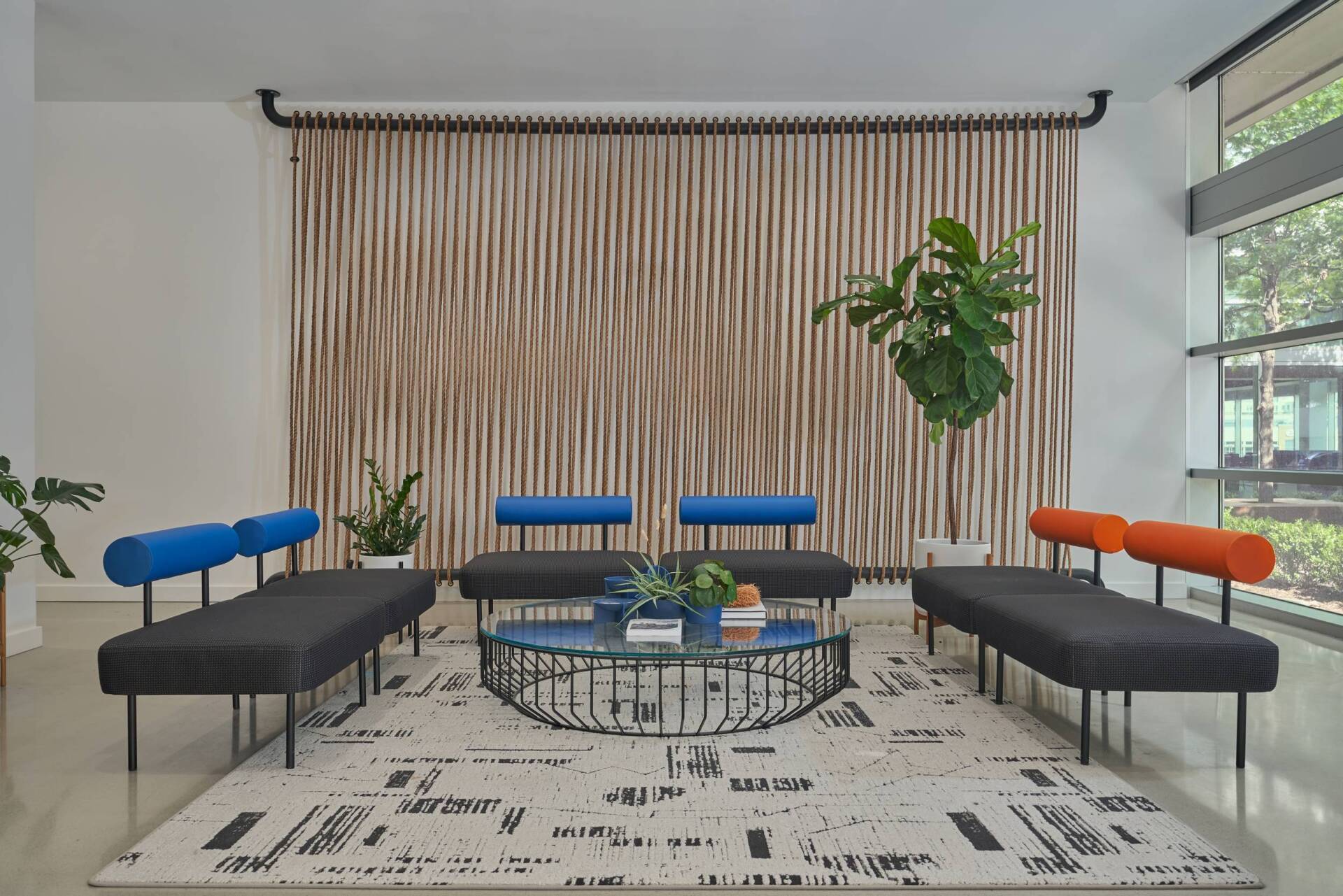Modern lounge area with gray and blue seating, large rug, and plant. A wall art is in the background.