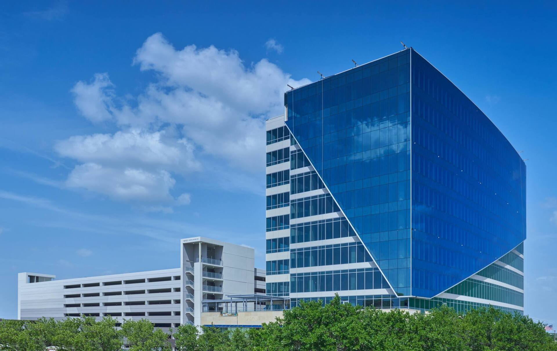 Modern blue glass office building with a unique angled facade against a blue sky.