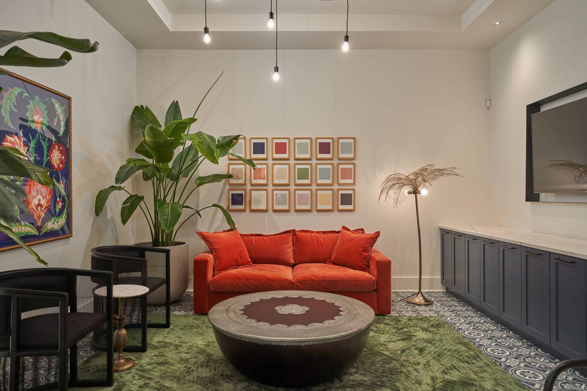 Cozy lounge with orange sofa, green rug, art, plants, and dark blue cabinets.