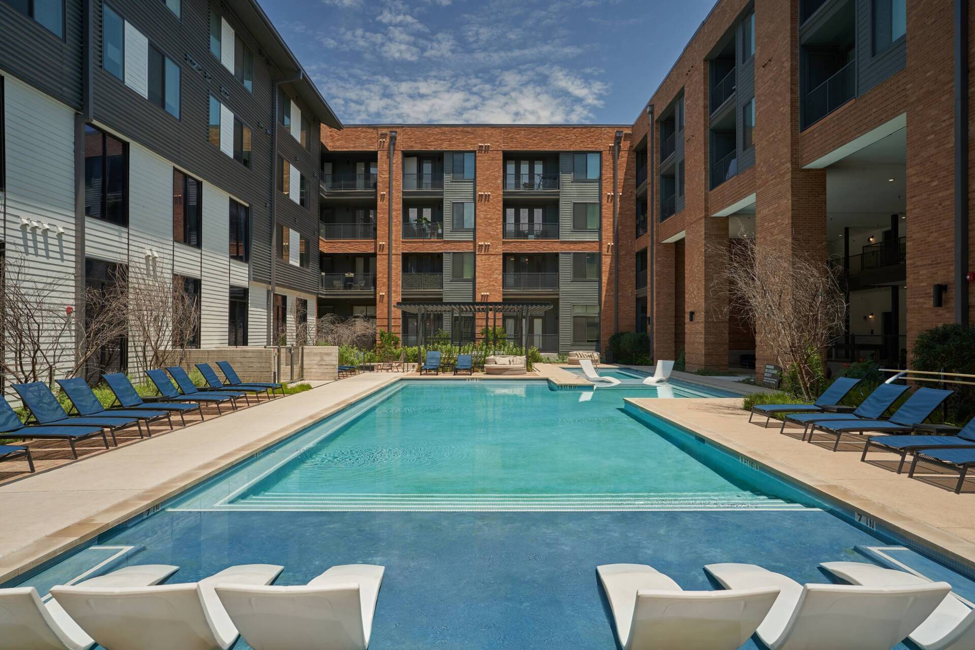 Pool surrounded by apartment buildings with blue lounge chairs.