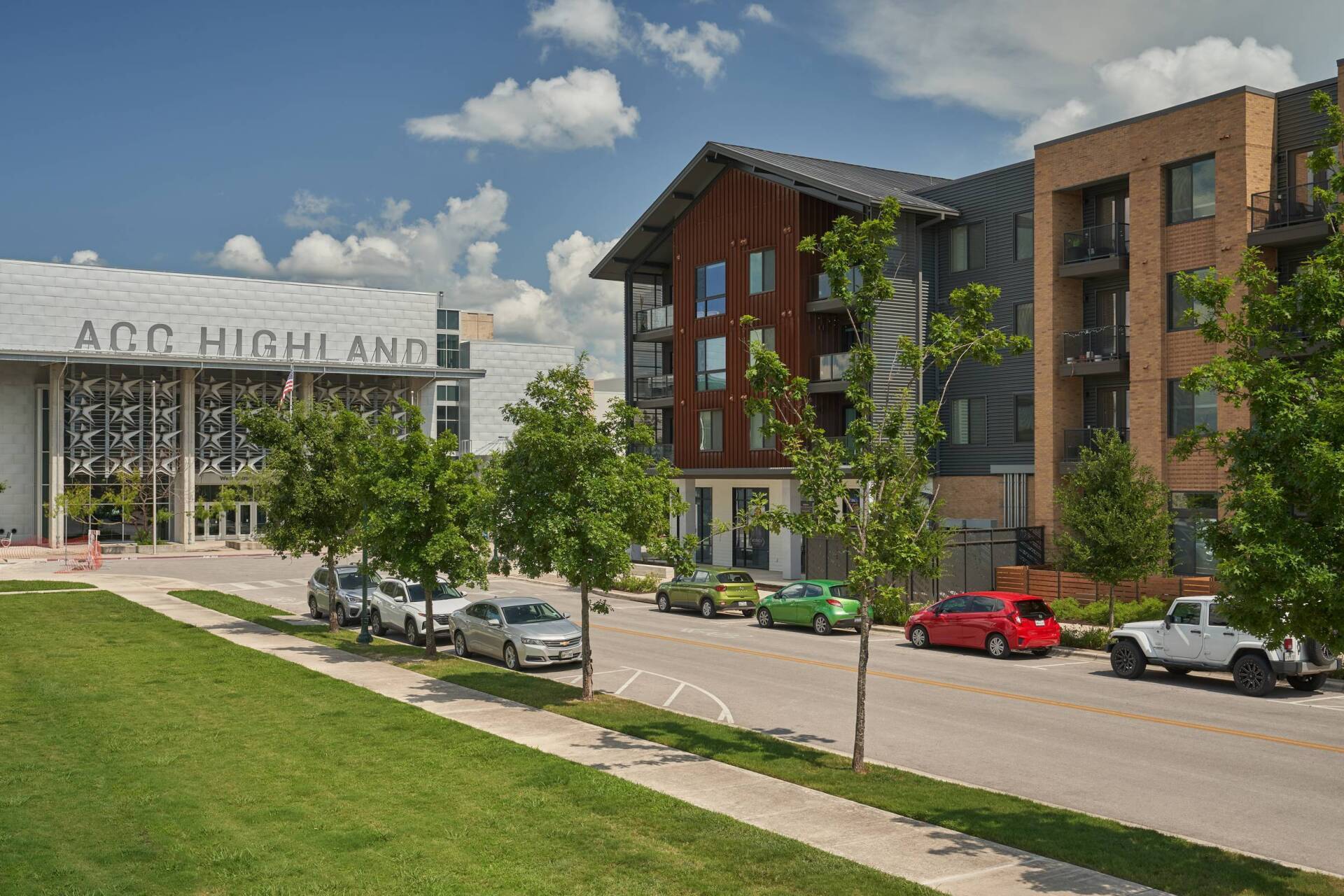 Street view of buildings, cars parked, green trees, and a grassy area with