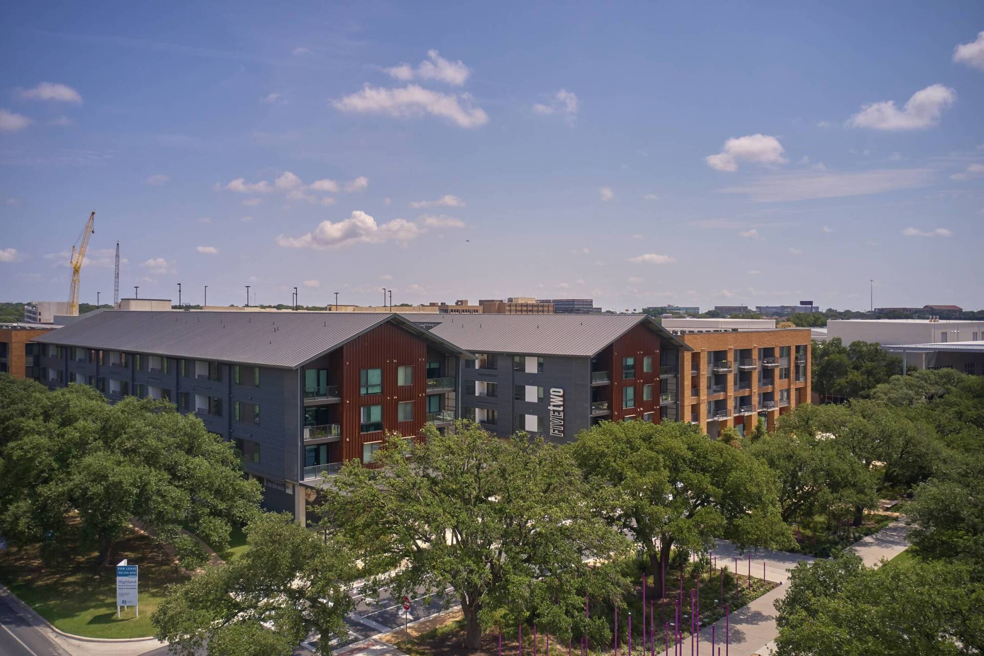Apartment complex with multiple buildings, trees, and a blue sky with clouds.