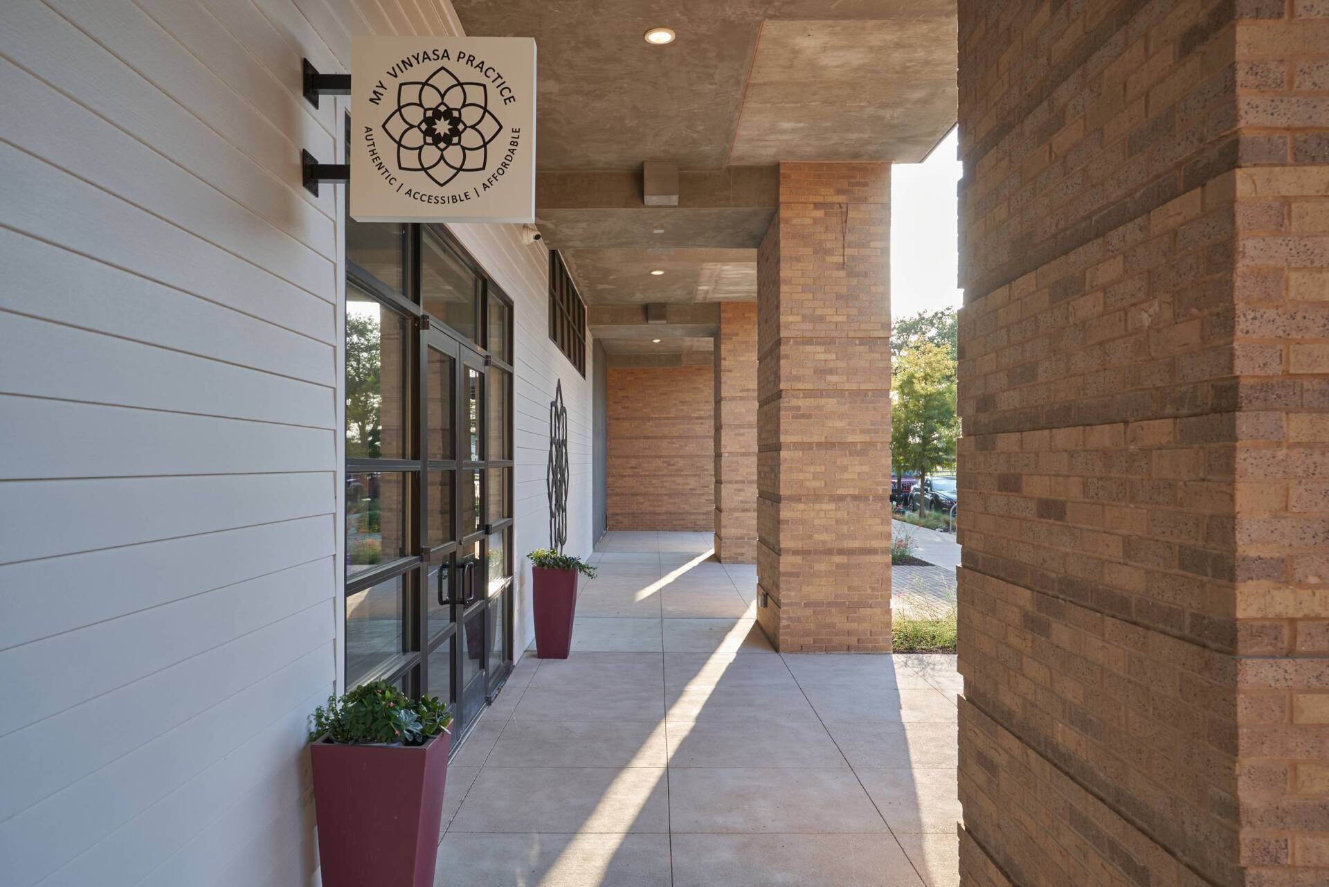 Exterior of a business with a sign. The entrance is under a covered walkway, flanked by brick columns and planters.