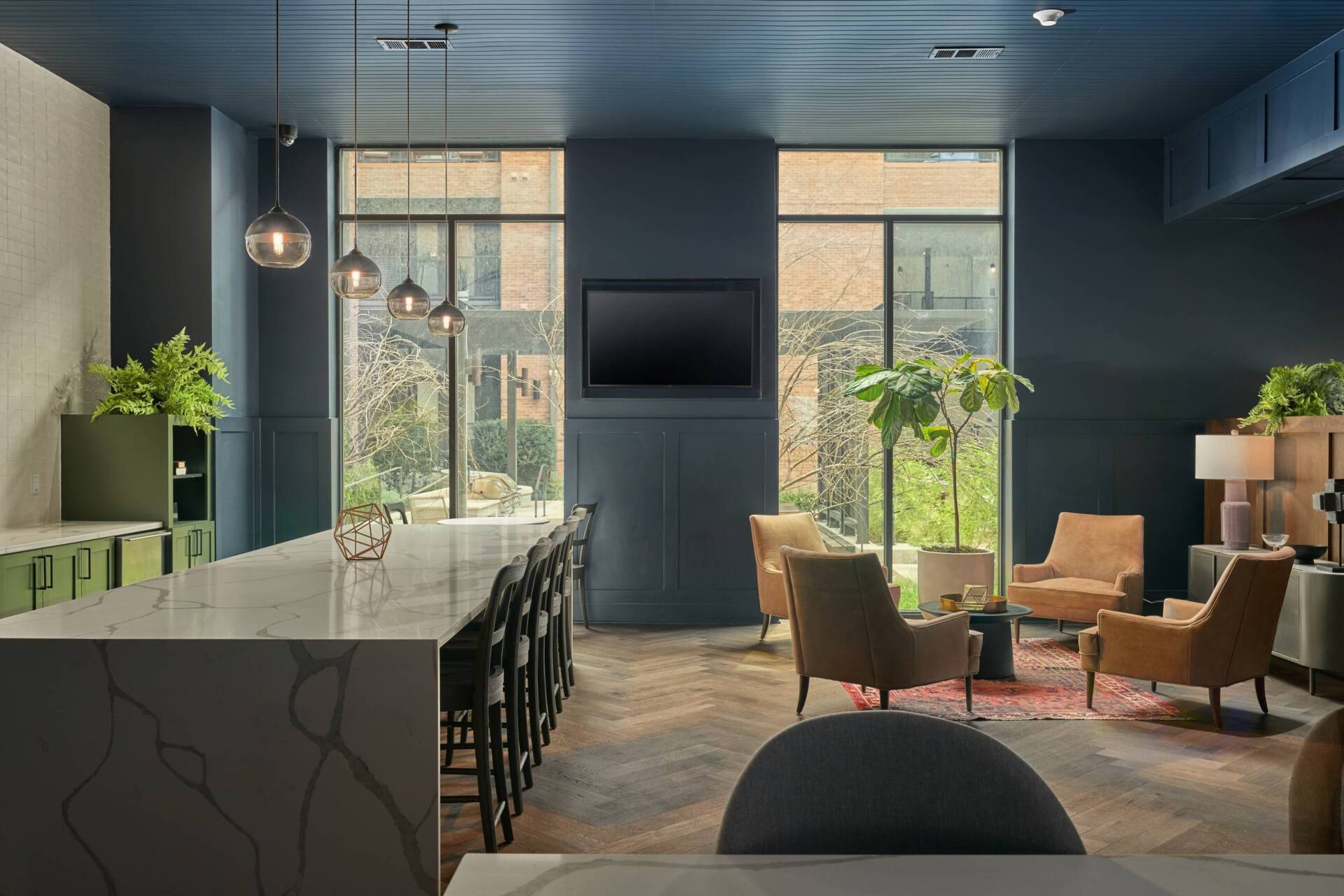 Modern lounge area with long bar, seating, large windows, dark blue walls, and plants.