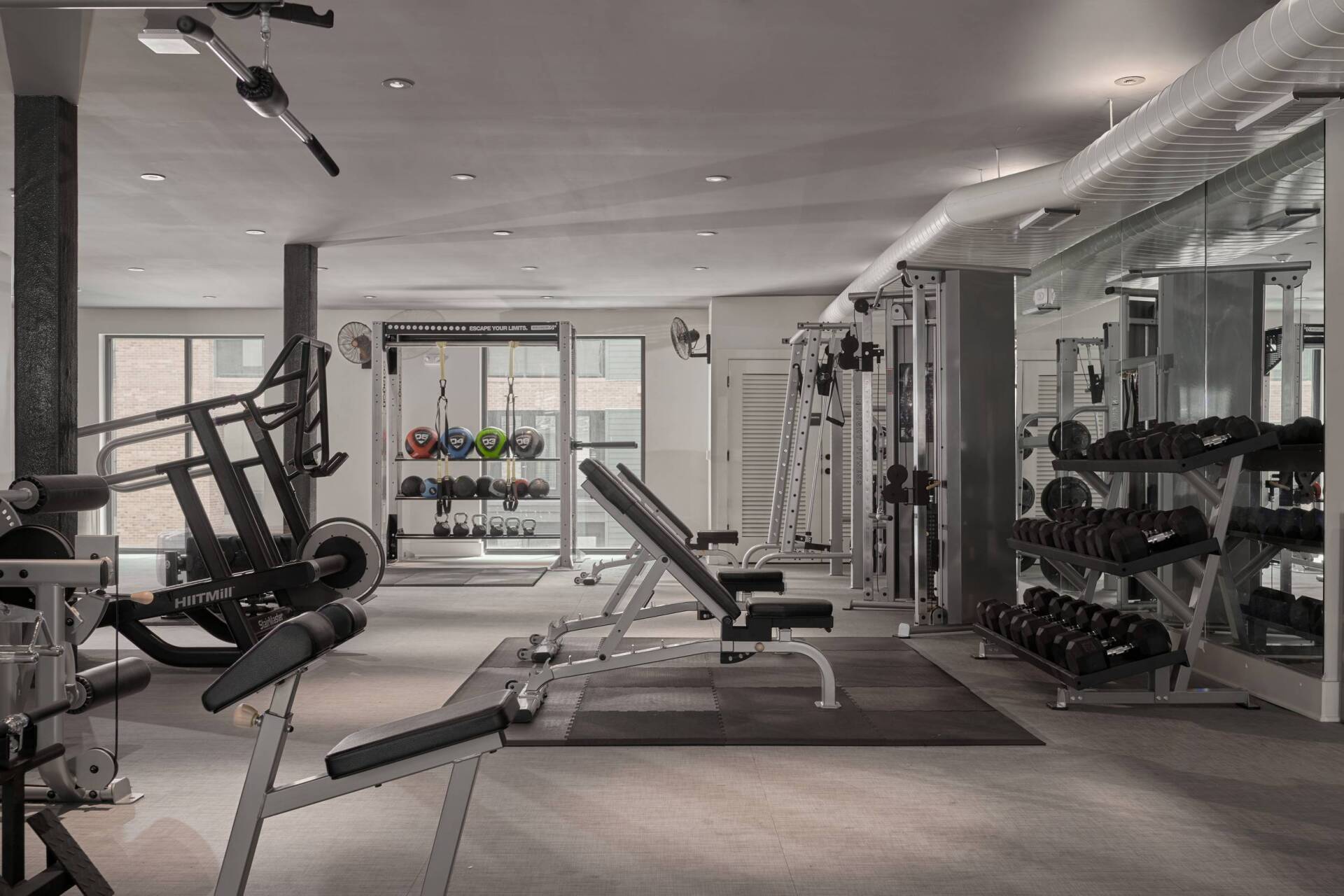 Gym interior with exercise equipment, including weight racks, benches, and machines.
