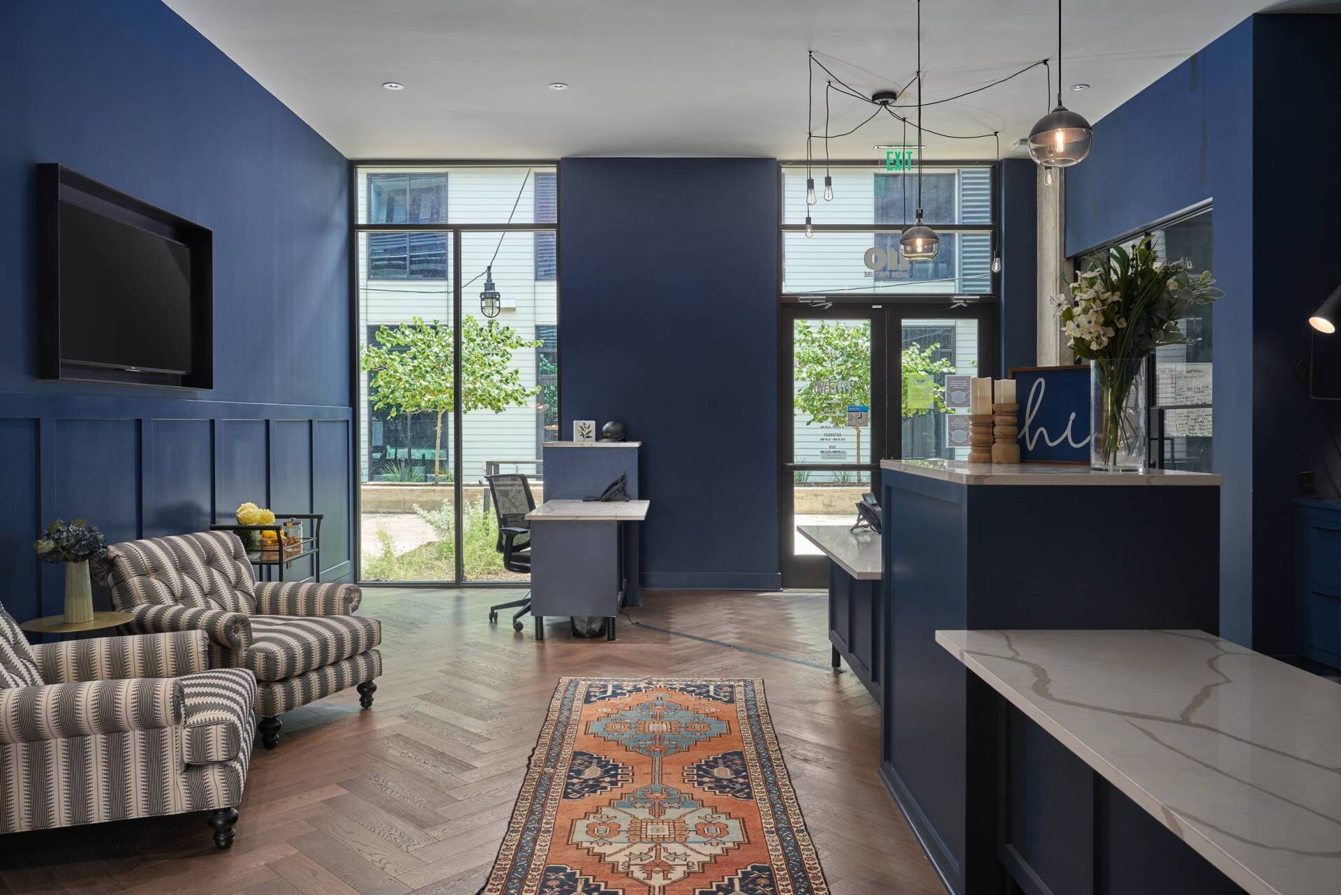 Blue-walled reception area with patterned chairs, a rug, large windows, and a reception desk.