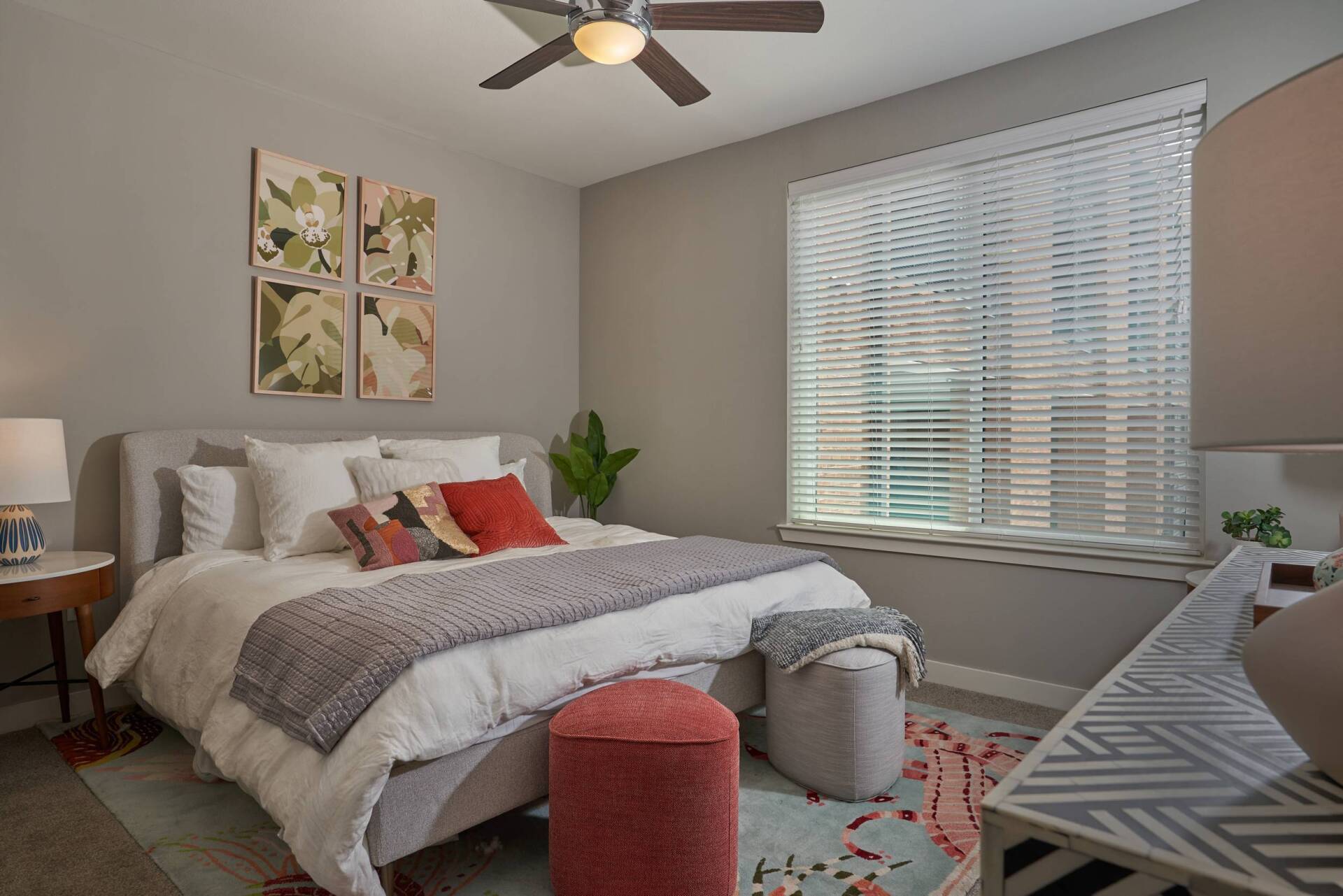 Bedroom with bed, side table, window with blinds, artwork, and gray walls.