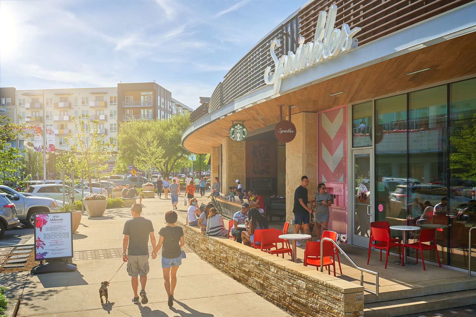 People walking and dining outside a retail store under a sunny sky.