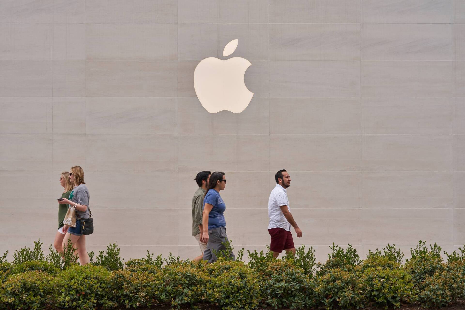 People walking in front of an Apple store with the Apple logo on the wall.