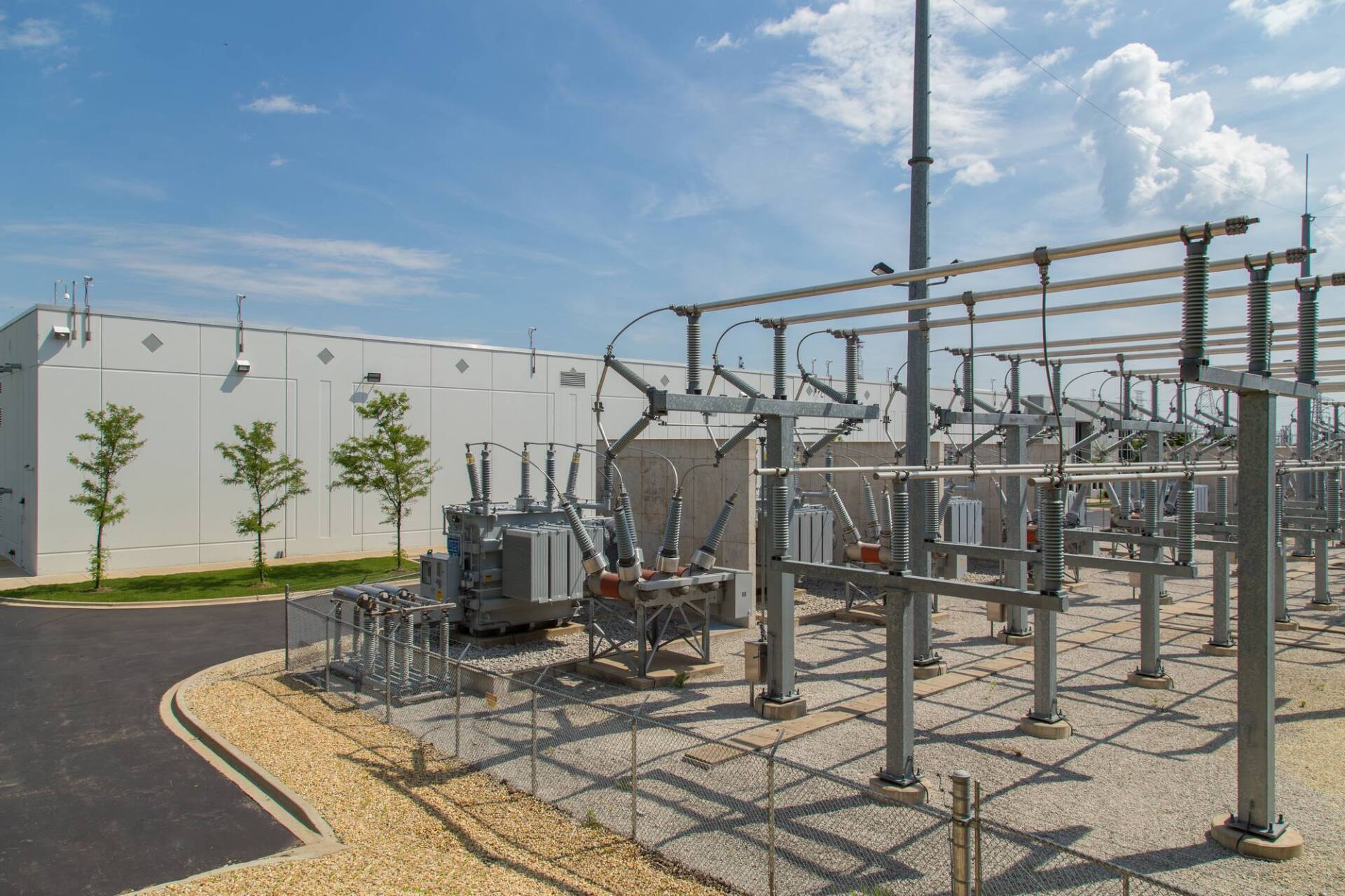 Electrical substation with transformers, equipment, and a white building under a blue sky.
