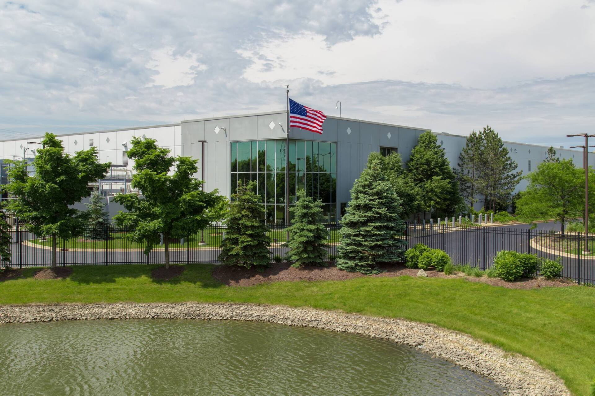 Building with glass entrance, American flag, trees, and pond.