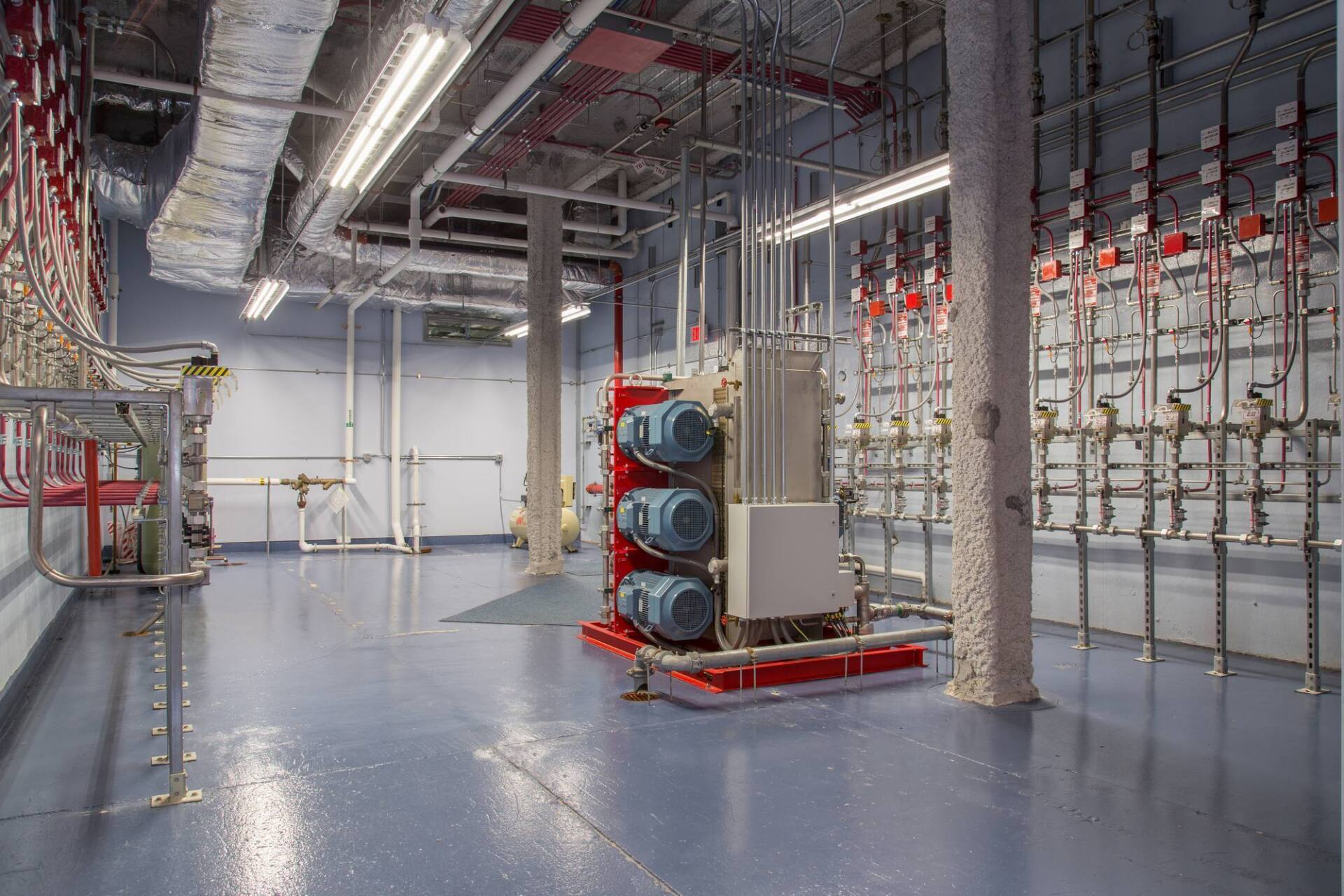 Mechanical room with pipes, electrical panels, and red and blue equipment on a blue floor.